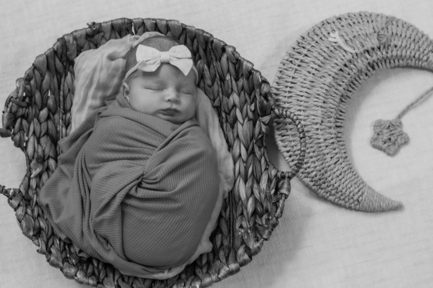 Black and white photo of swaddled newborn in basket with decorative moon accent.