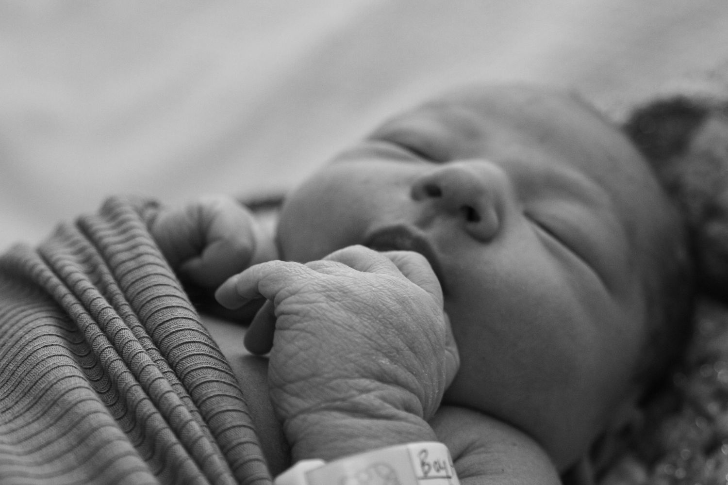Close-up black and white portrait of sleeping newborn with hospital identification band.