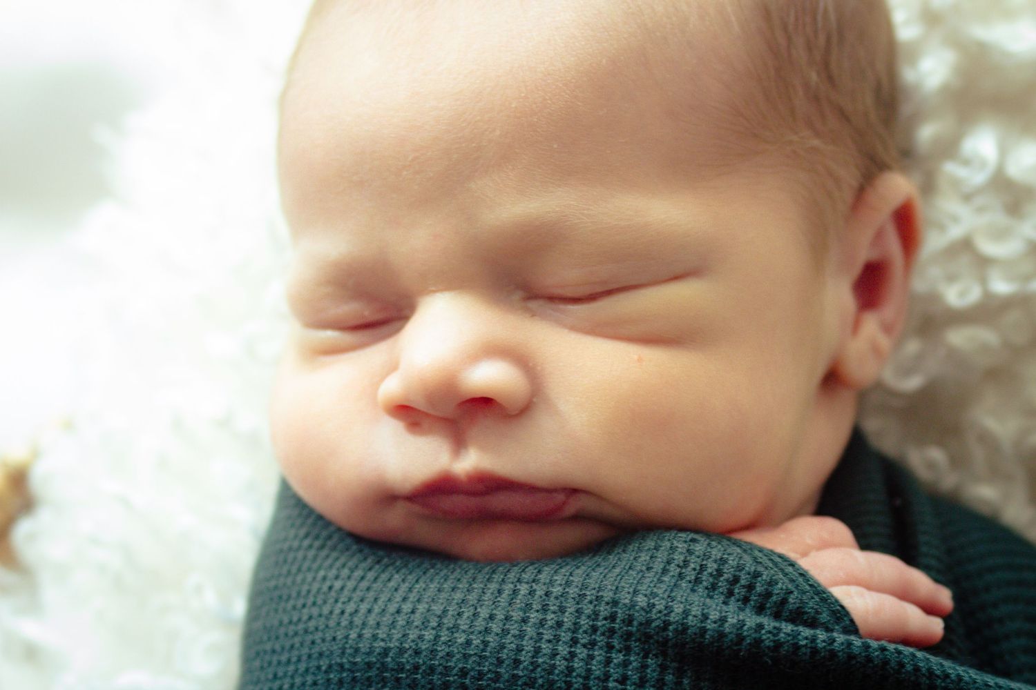 Peaceful sleeping newborn rests against teal blanket with soft lighting.