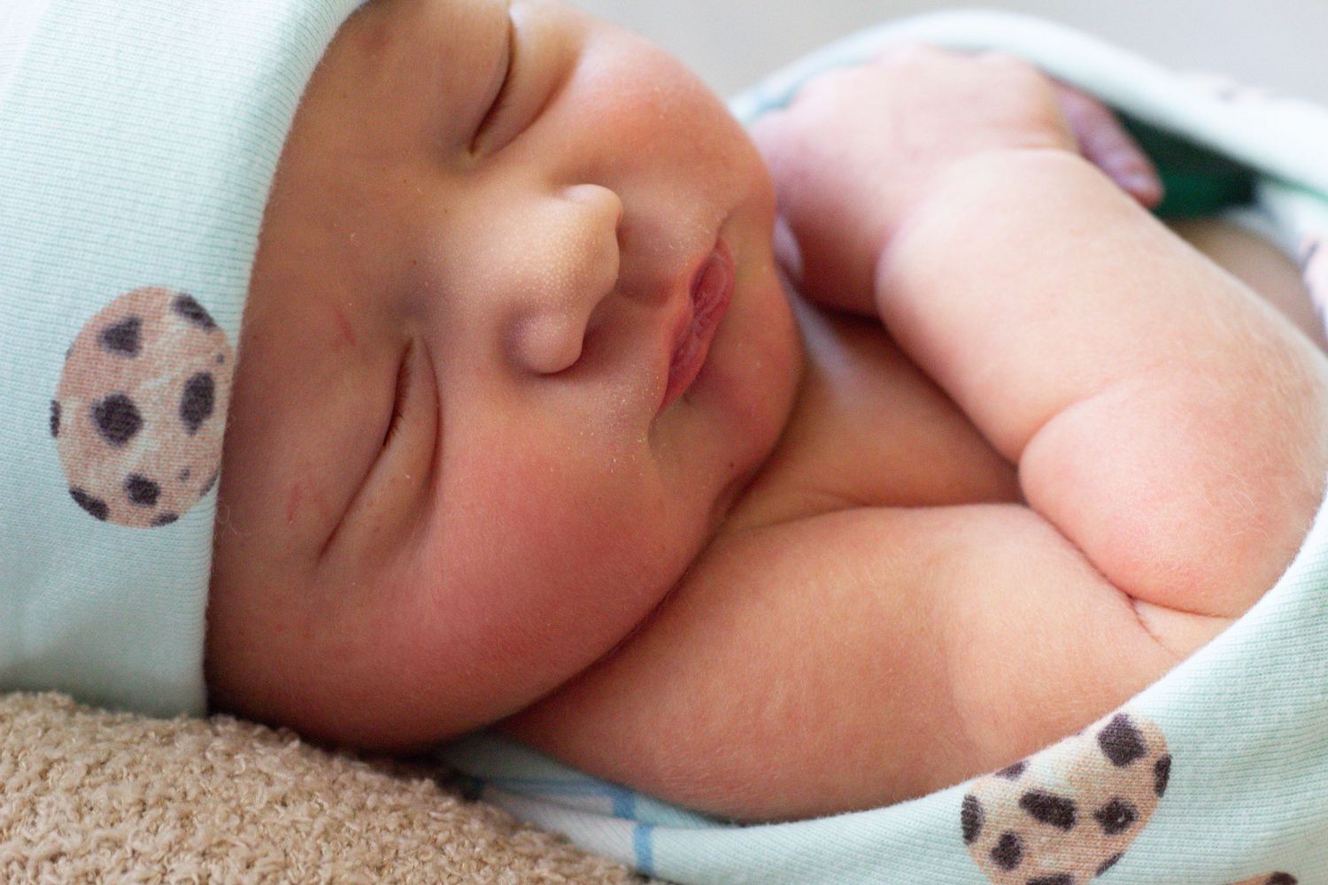 Sleeping newborn wearing a light blue hat with polka dots.