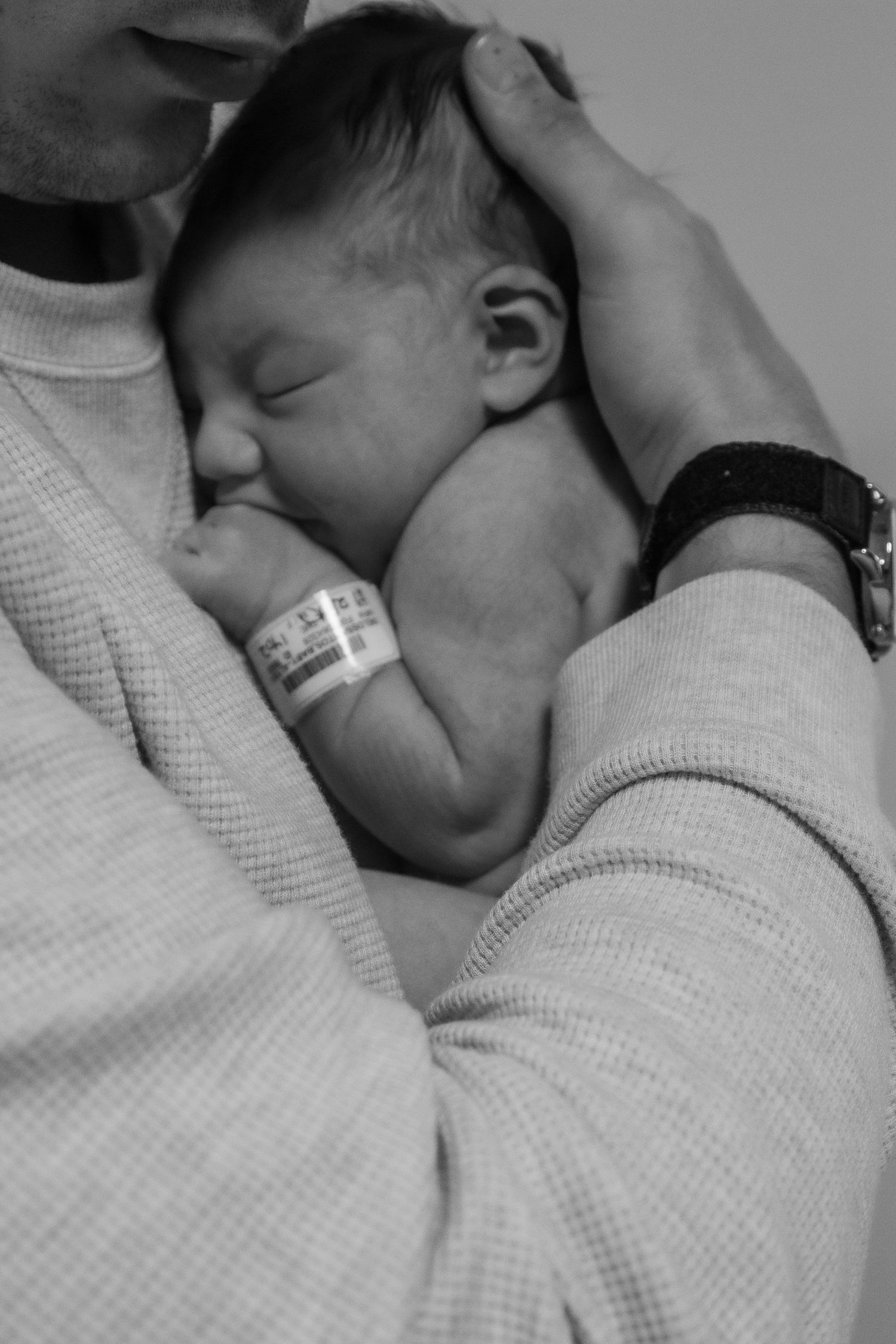 Black and white image of sleeping newborn with hospital bracelet being cradled.