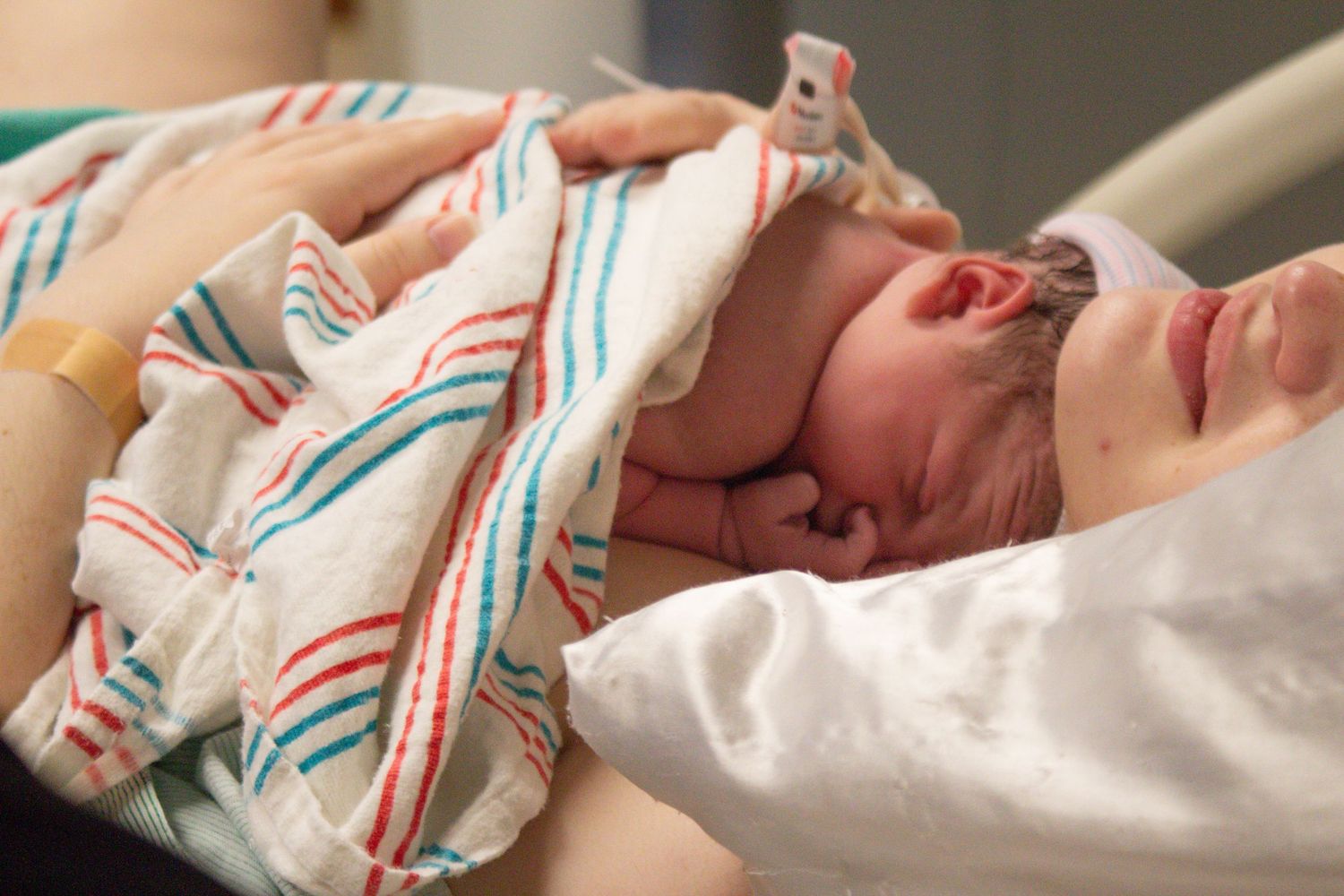 Newborn baby wrapped in a striped hospital blanket crying moments after birth.
