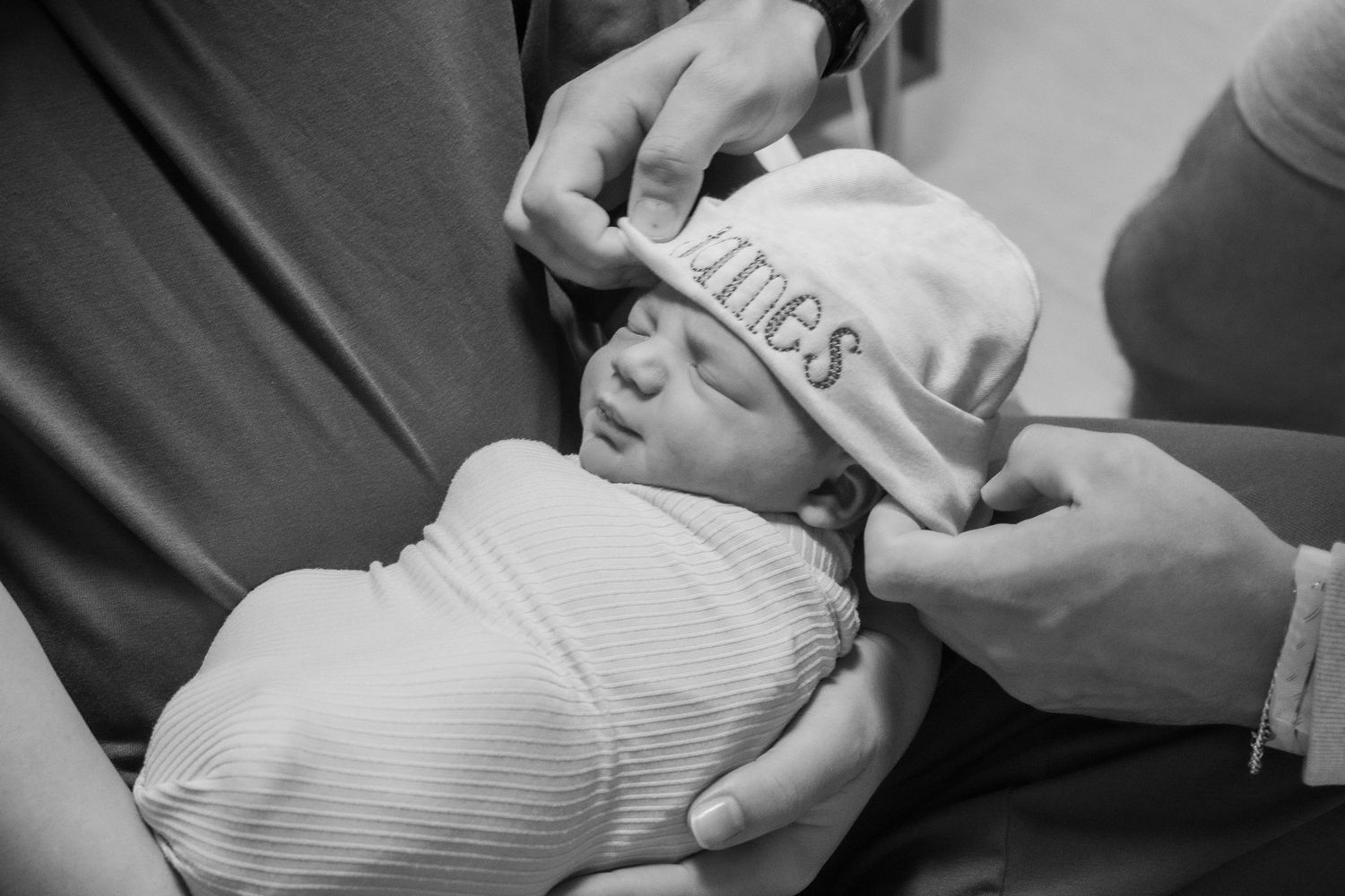 A newborn baby wearing a white cap being held during a tender hospital moment.