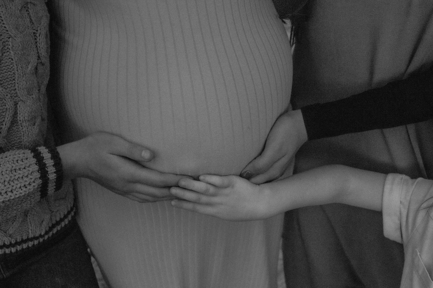 Close-up shot of hands gently touching a pregnant belly in black and white.