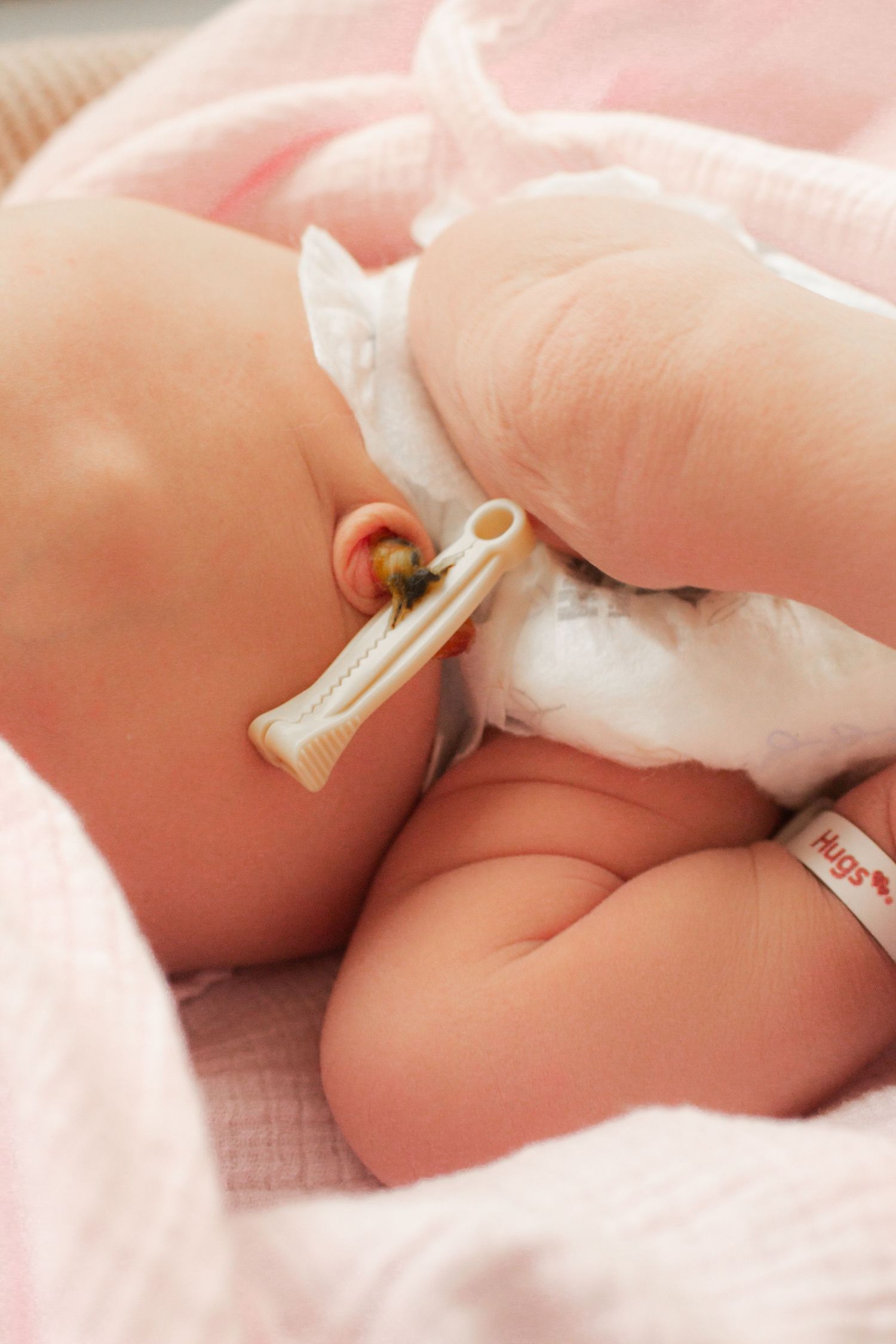 Close-up of newborn baby's ear with temperature monitor in soft pink surroundings.