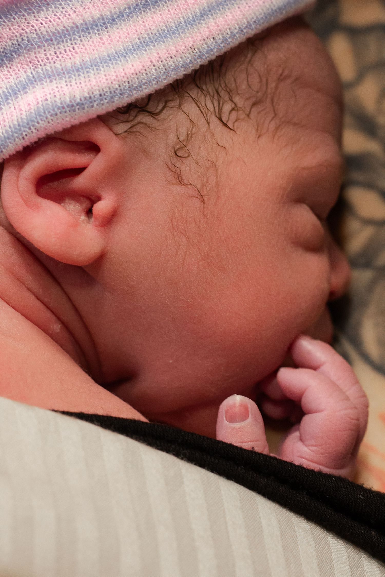 Close-up of sleeping newborn with striped hat and wispy hair.