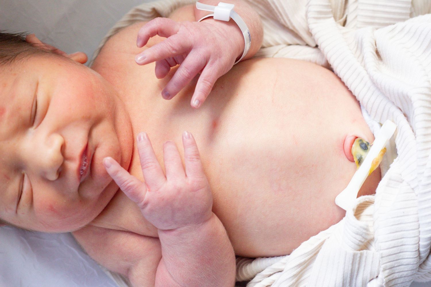 A sleeping newborn rests peacefully with tiny hands curled near their face.