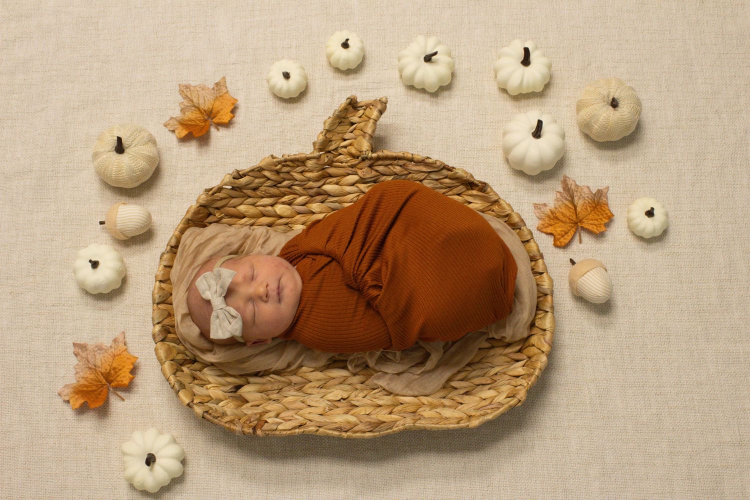 Autumn themed newborn portrait with white pumpkins and maple leaves around woven basket.