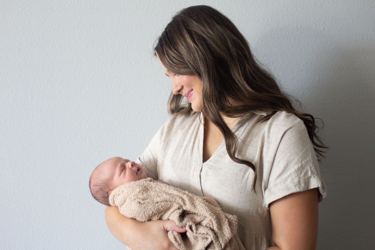 Tender moment as caregiver in light clothing cradles sleeping newborn wrapped in beige blanket.