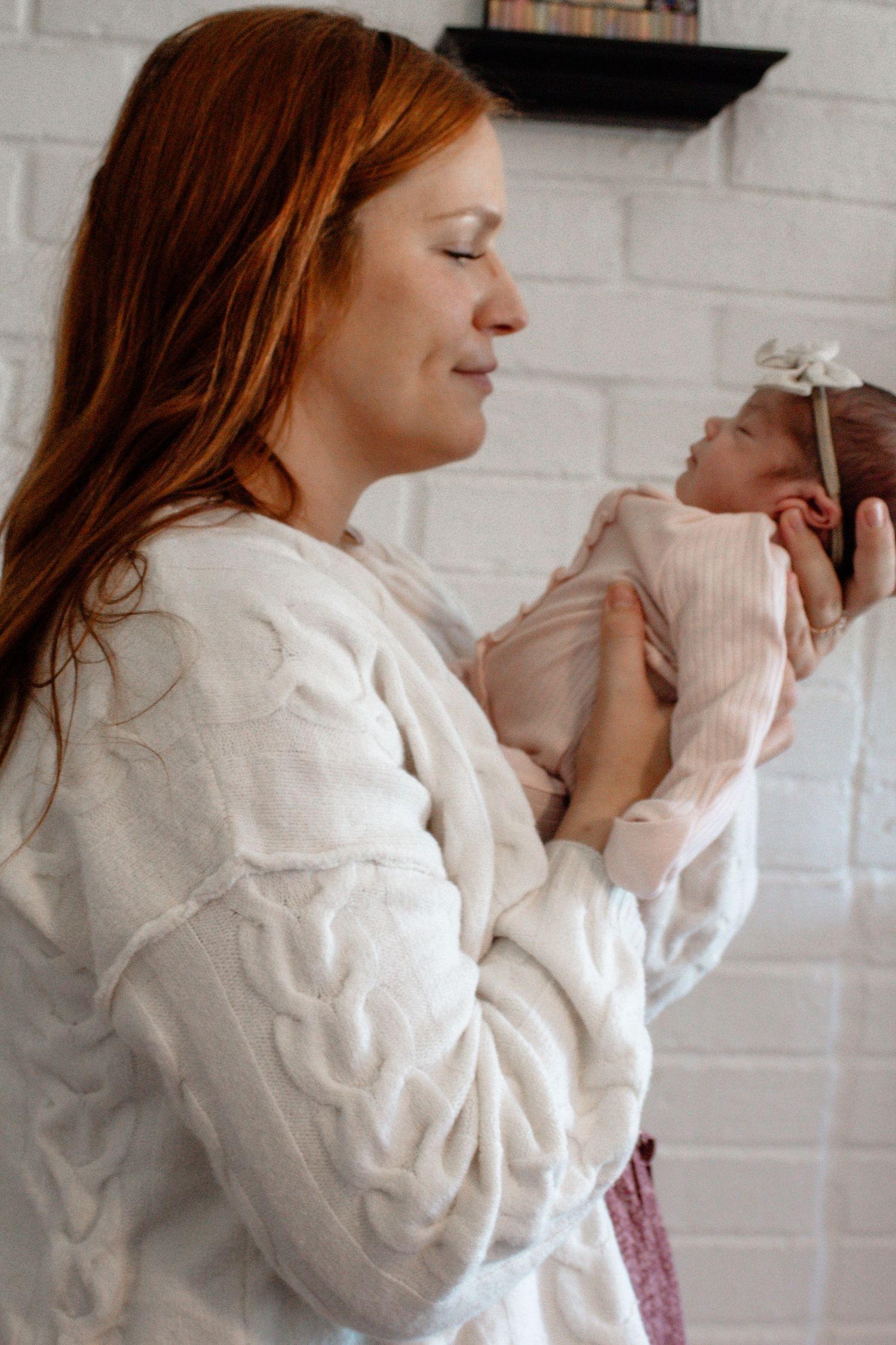 Parent in white sweater holding and gazing lovingly at swaddled newborn.