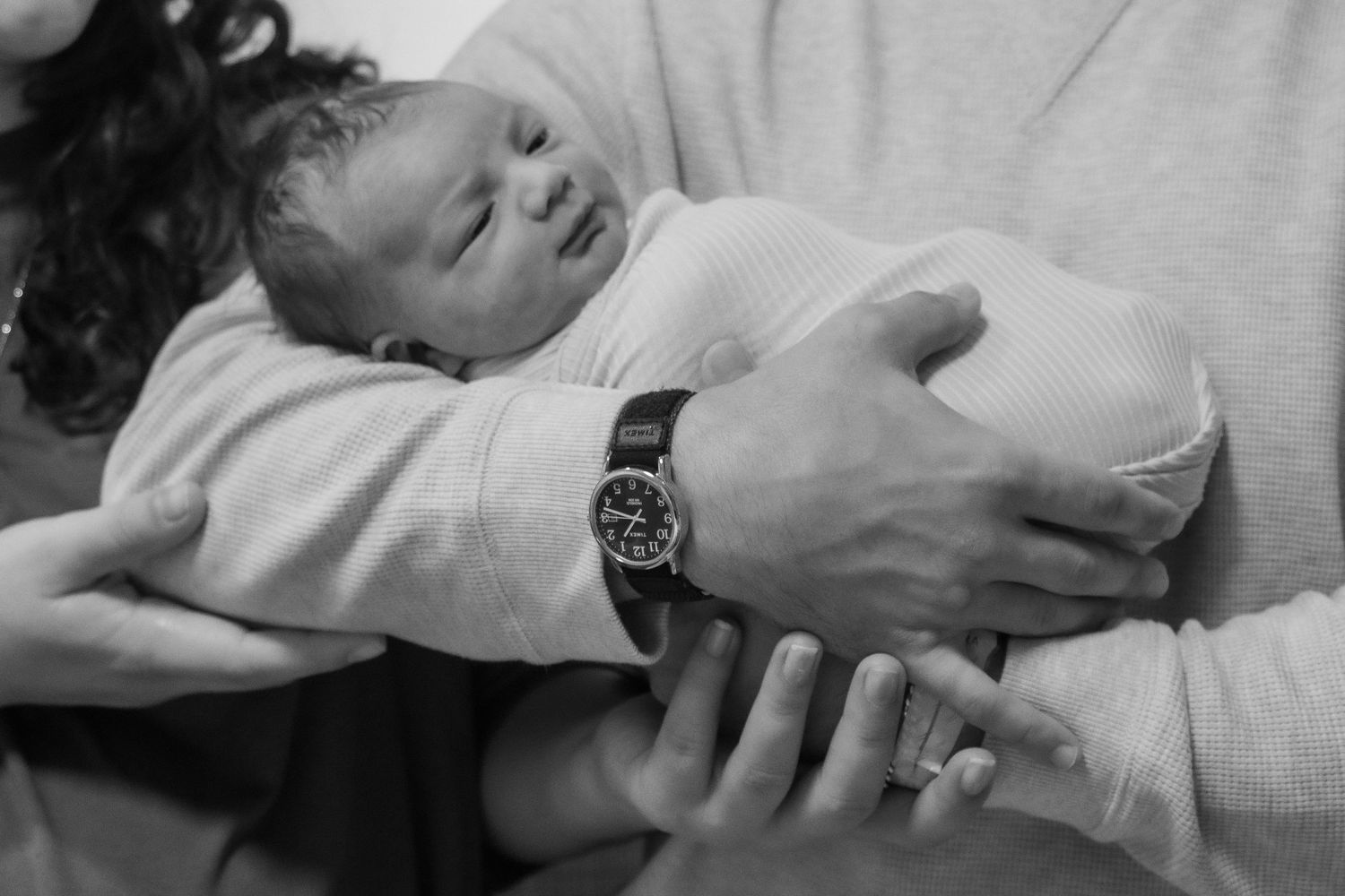 A black and white photo of a peaceful newborn being held in protective arms.