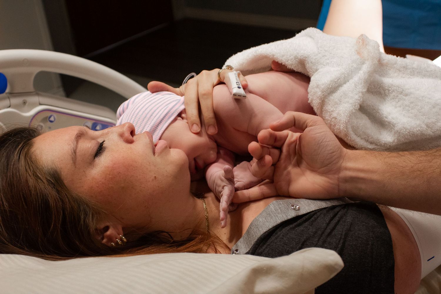 A newborn baby rests on an adult's chest during skin-to-skin bonding after birth in a medical setting.