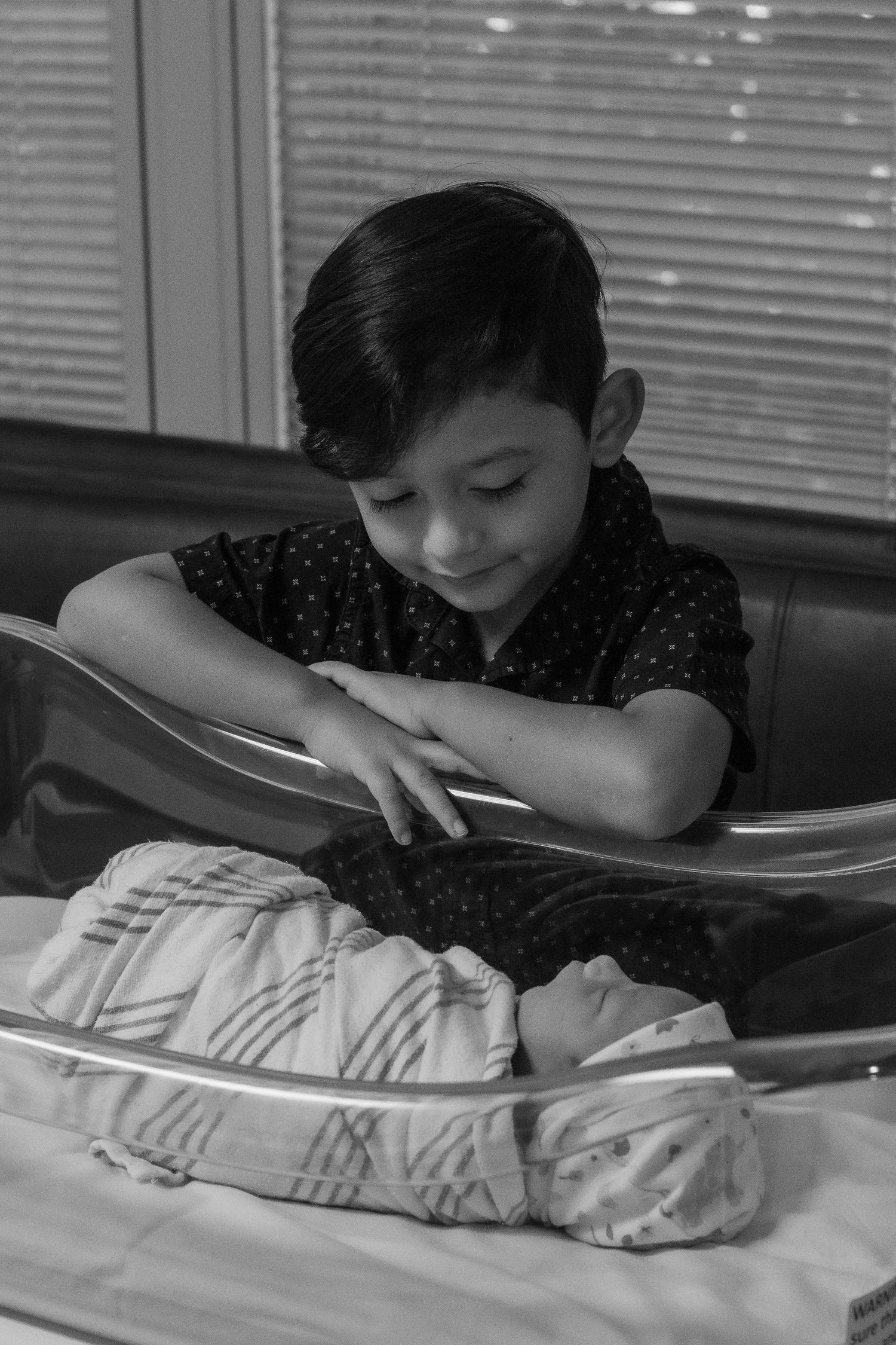 Sibling watching newborn baby sleeping in hospital bassinet.