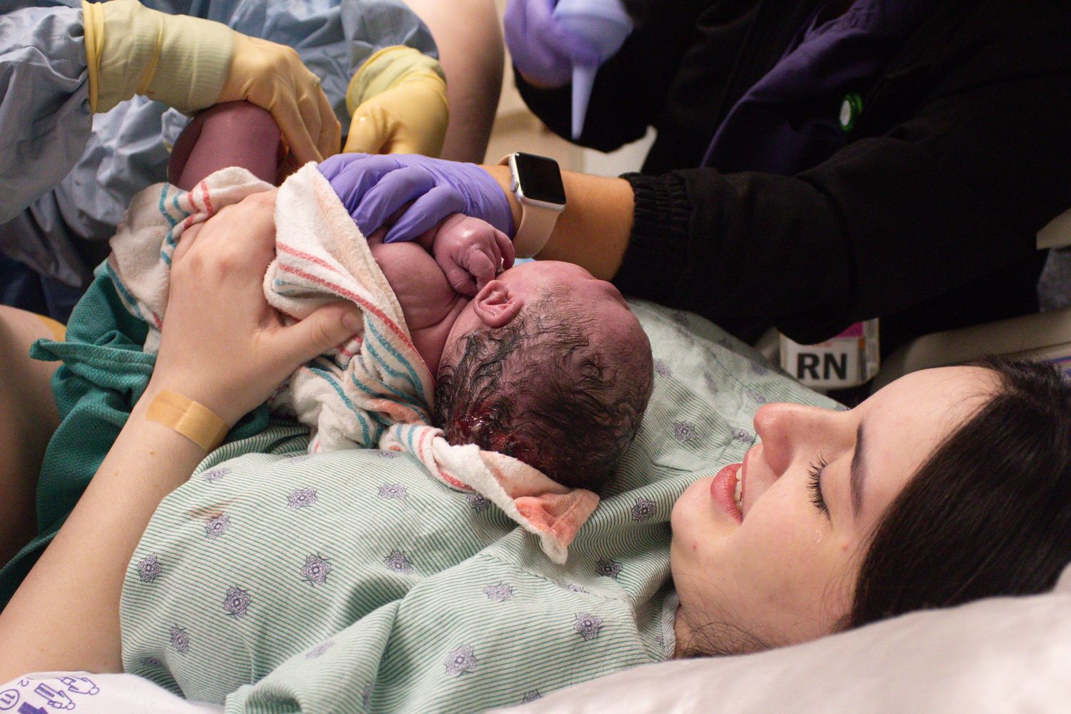 Healthcare providers examining newborn immediately after birth in delivery room.