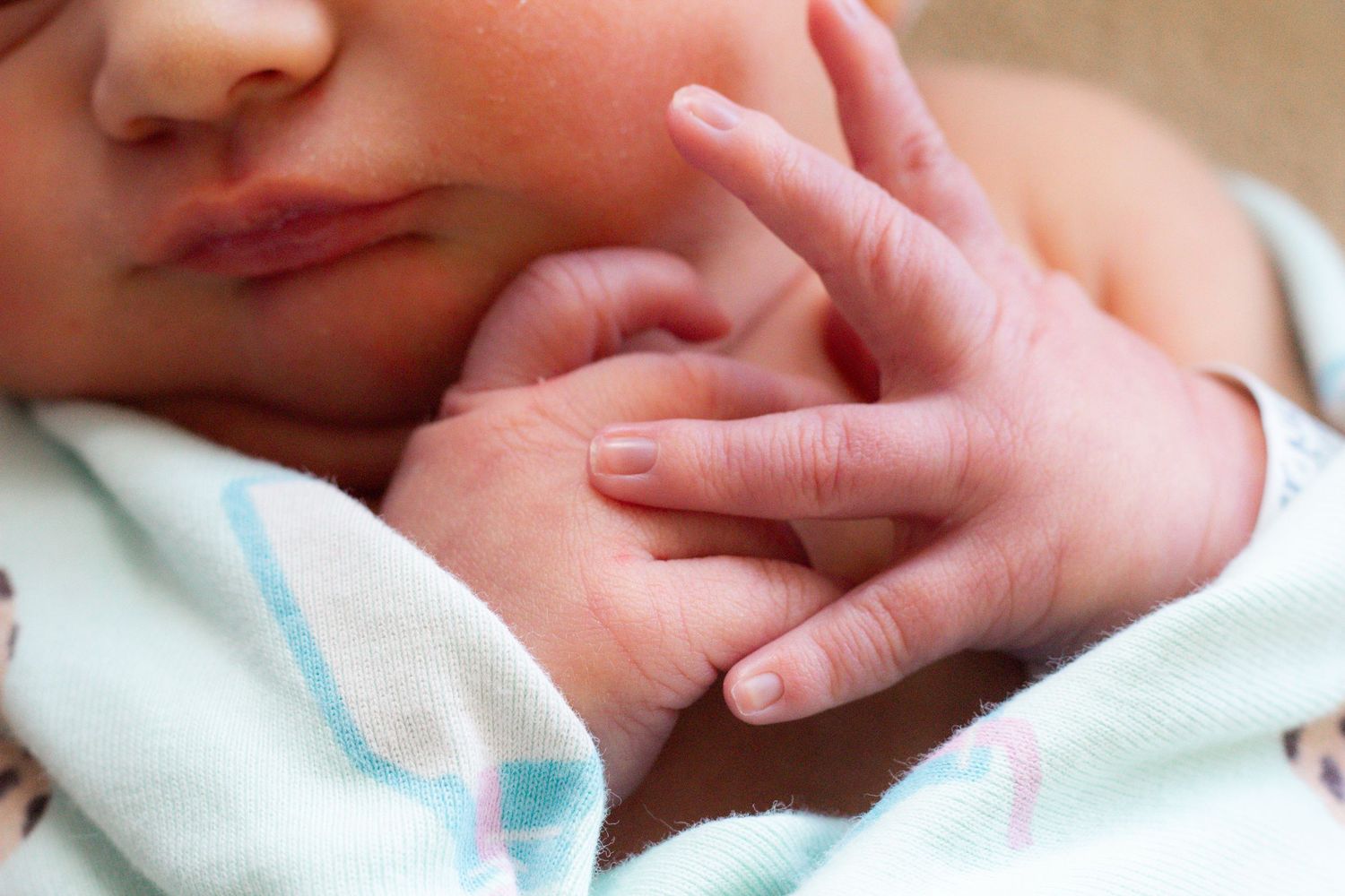 Close-up shot of a baby's tiny hand wrapped in a blue and pink striped blanket.