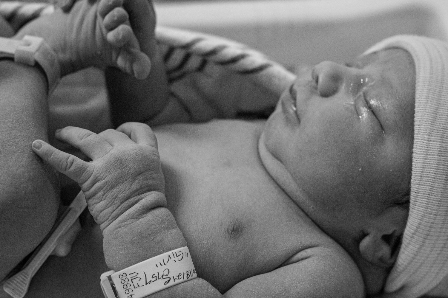 Close-up black and white portrait of newborn infant with hospital ID bracelet.