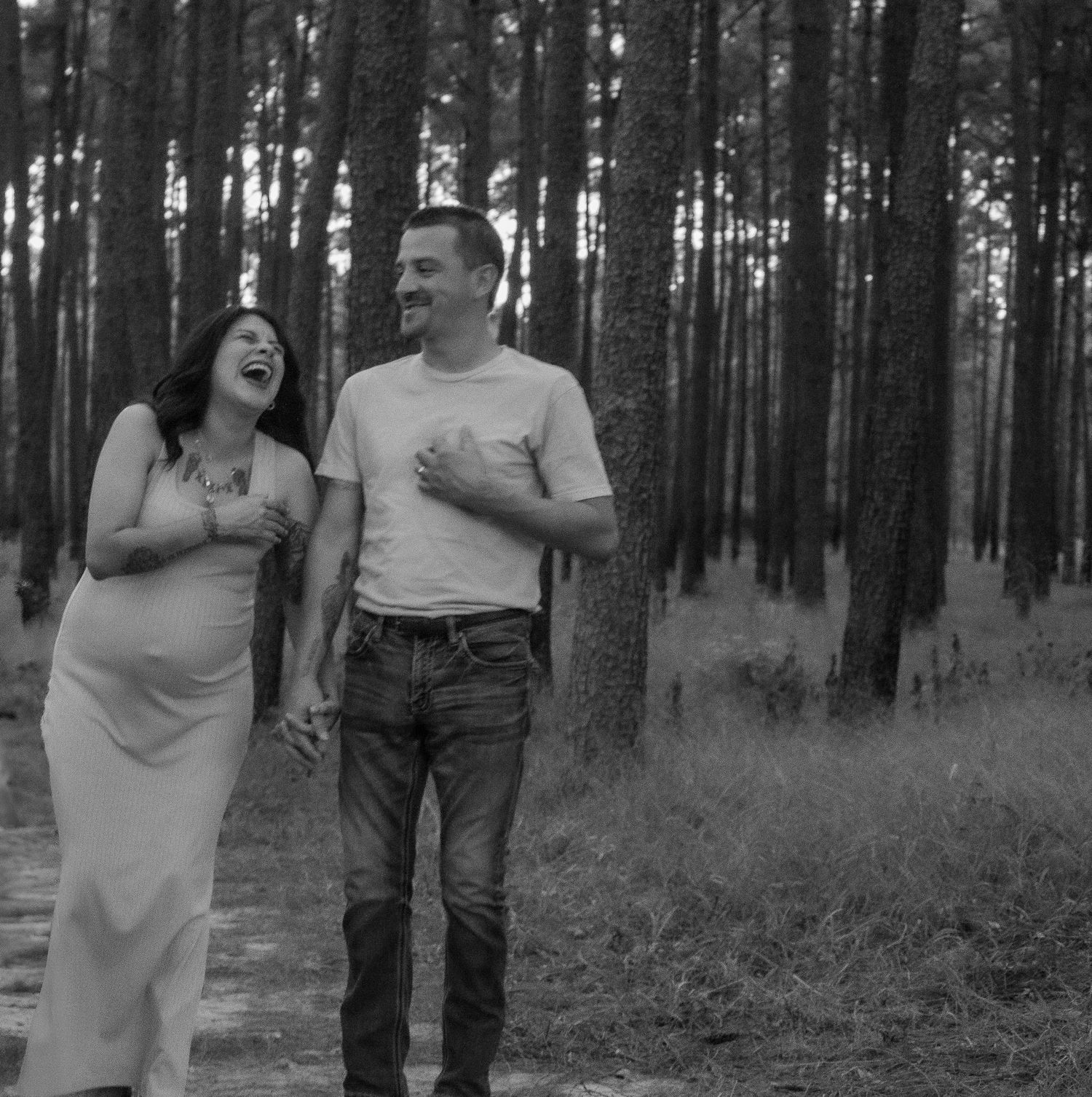 Joyful couple laugh together during forest maternity photoshoot.