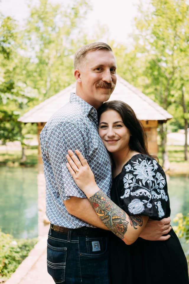 Happy couple embracing outdoors with gazebo and pond in background.