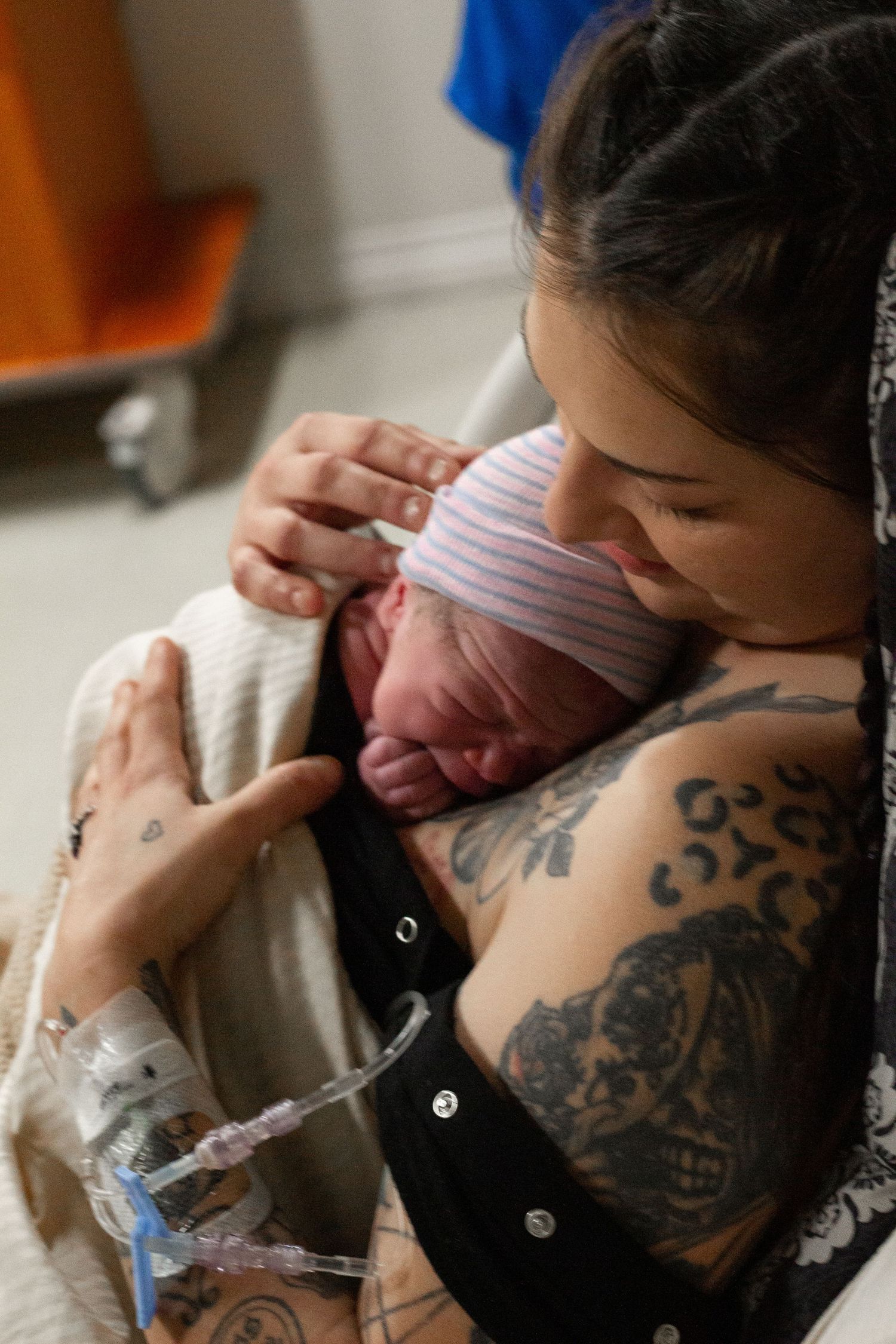 Newborn baby being cradled close while bonding with parent showing ornate tattoo sleeve.