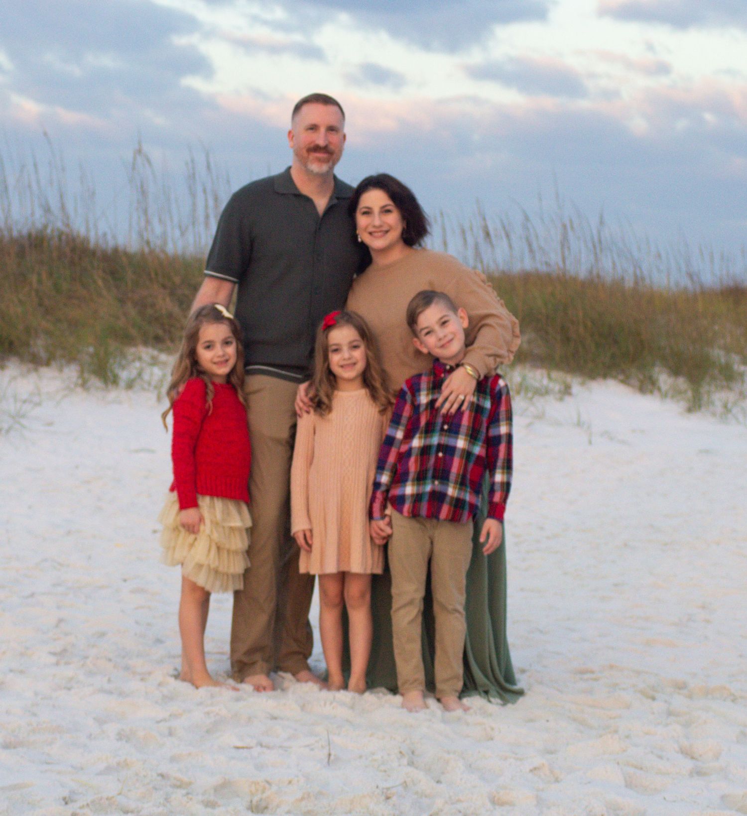 Happy family of five posing together on a sandy beach at sunset.