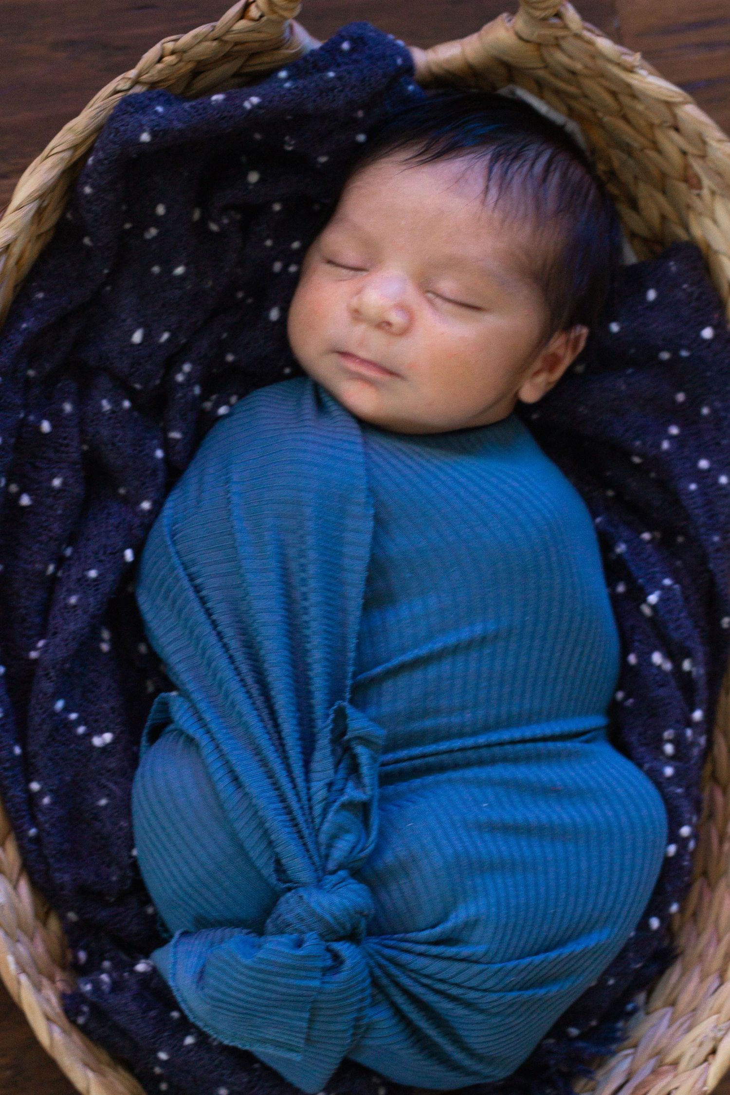Newborn sleeping in woven basket with blue outfit and starry blanket.