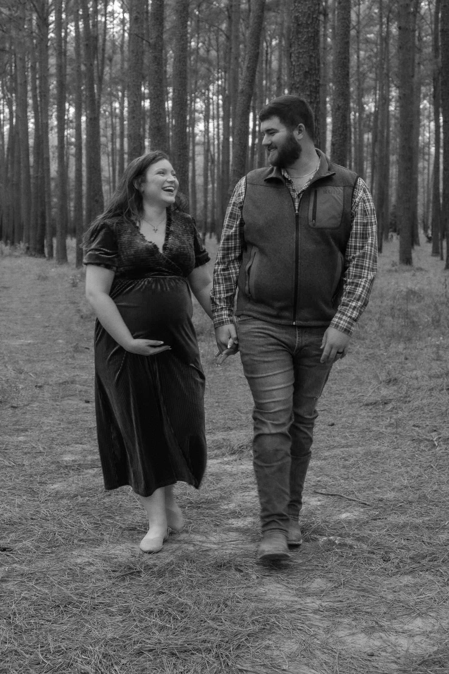 Couple walking together through pine forest during maternity photoshoot.