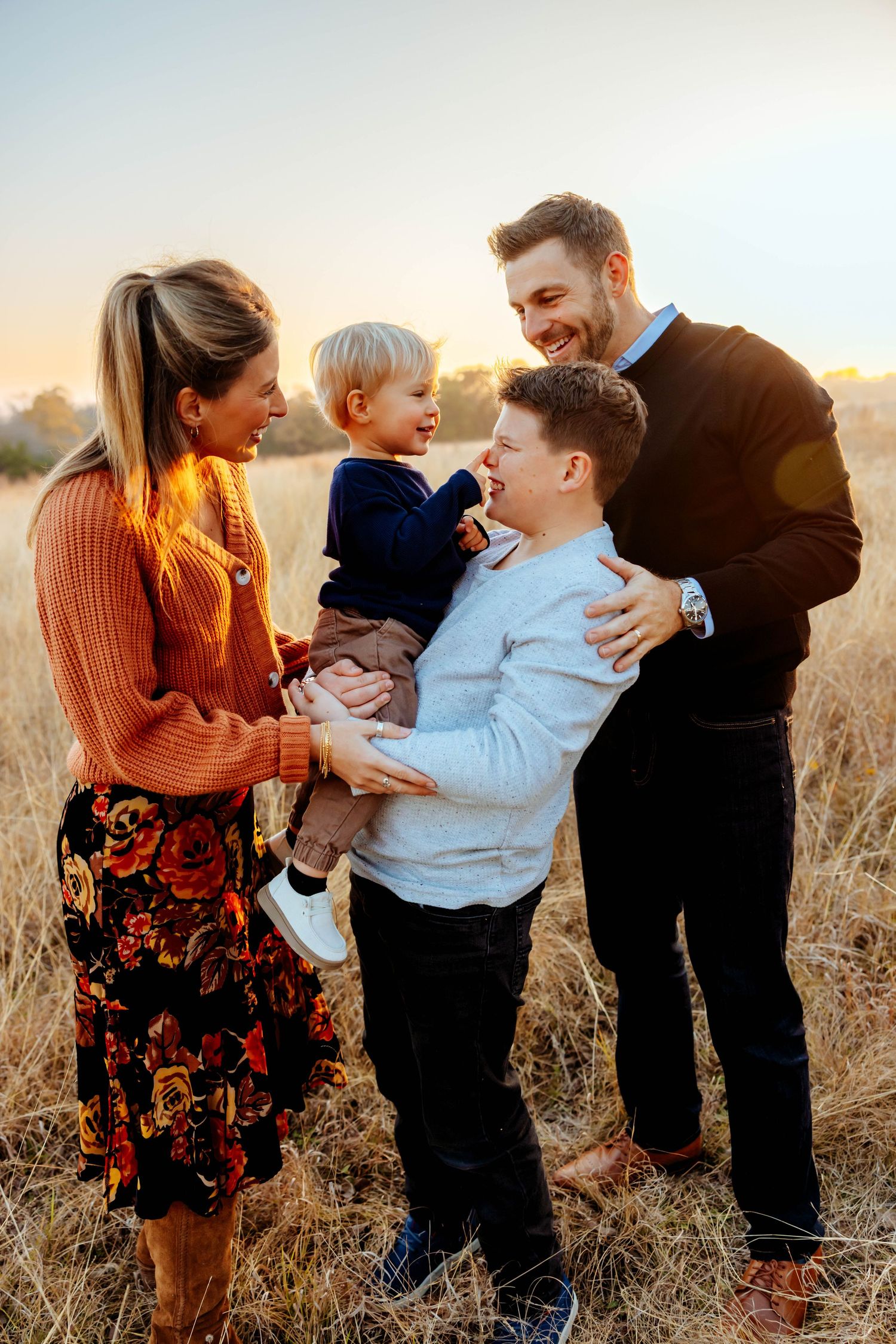 A family shares tender moments together in a golden wheat field at sunset.
