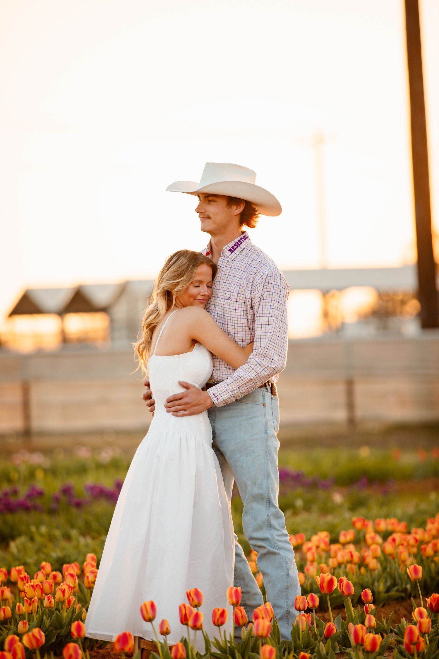 A romantic couple embraces in a field of orange tulips at sunset while wearing western attire and formal dress.