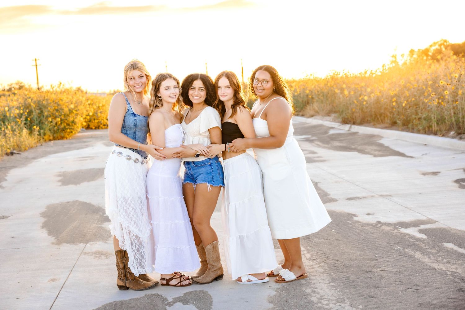 Group of high school senior girls standing together at sunset, laughing and hugging during a styled senior rep team photoshoot