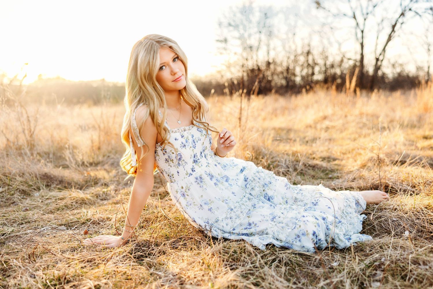 A person in a floral dress lies gracefully in a sunlit meadow during golden hour.