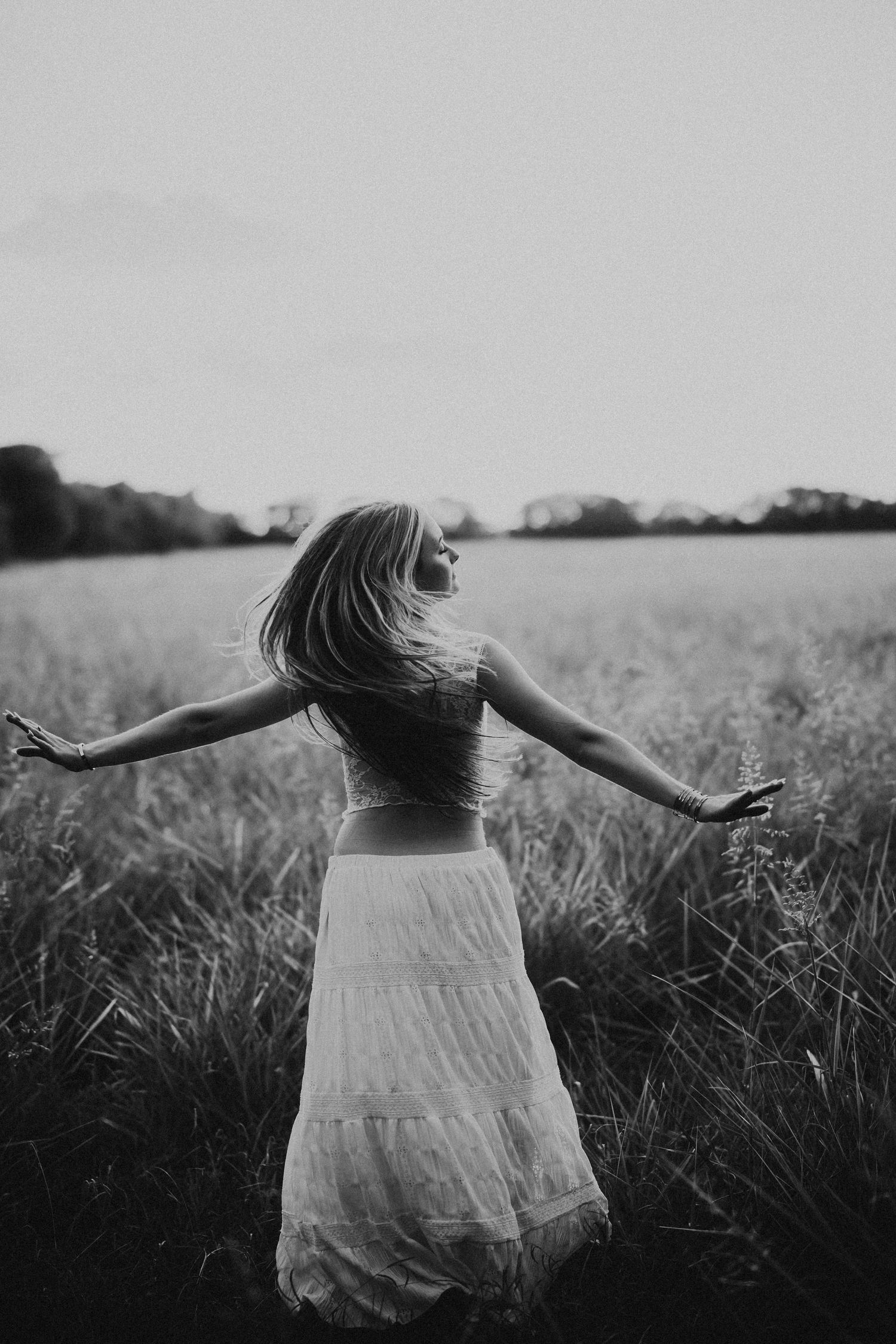 Black and white photo of a woman in a white skirt with arms outstretched in an open field.