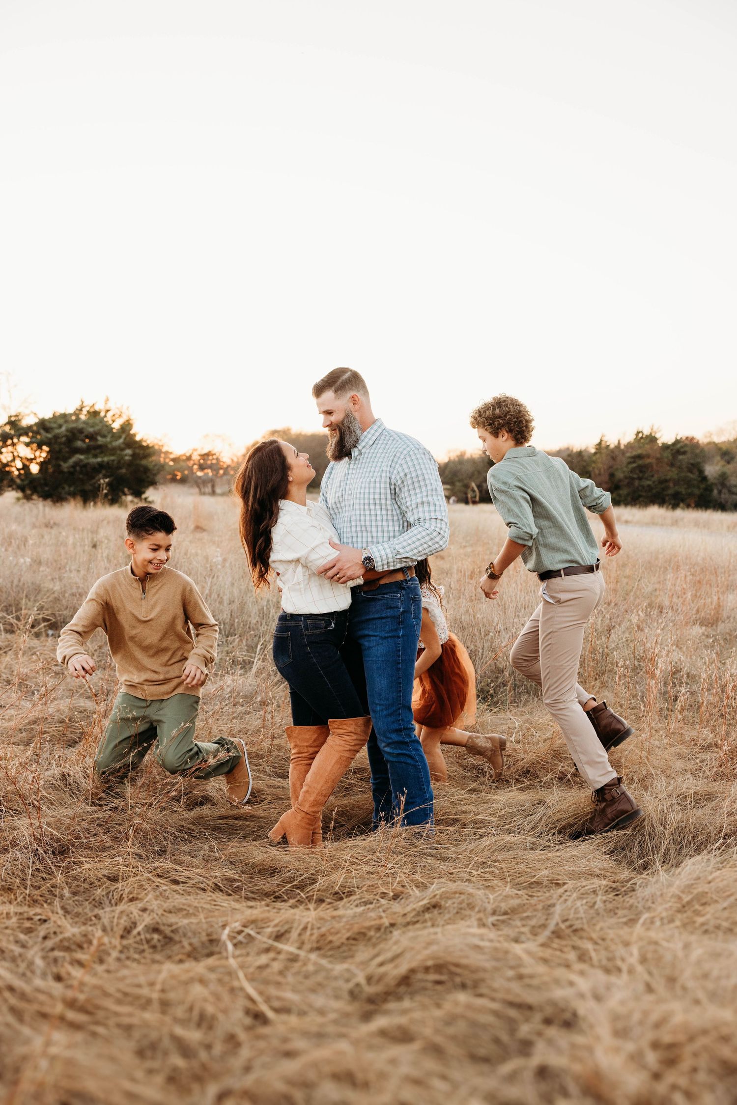 Family plays and laughs together in a golden sunlit field during sunset.