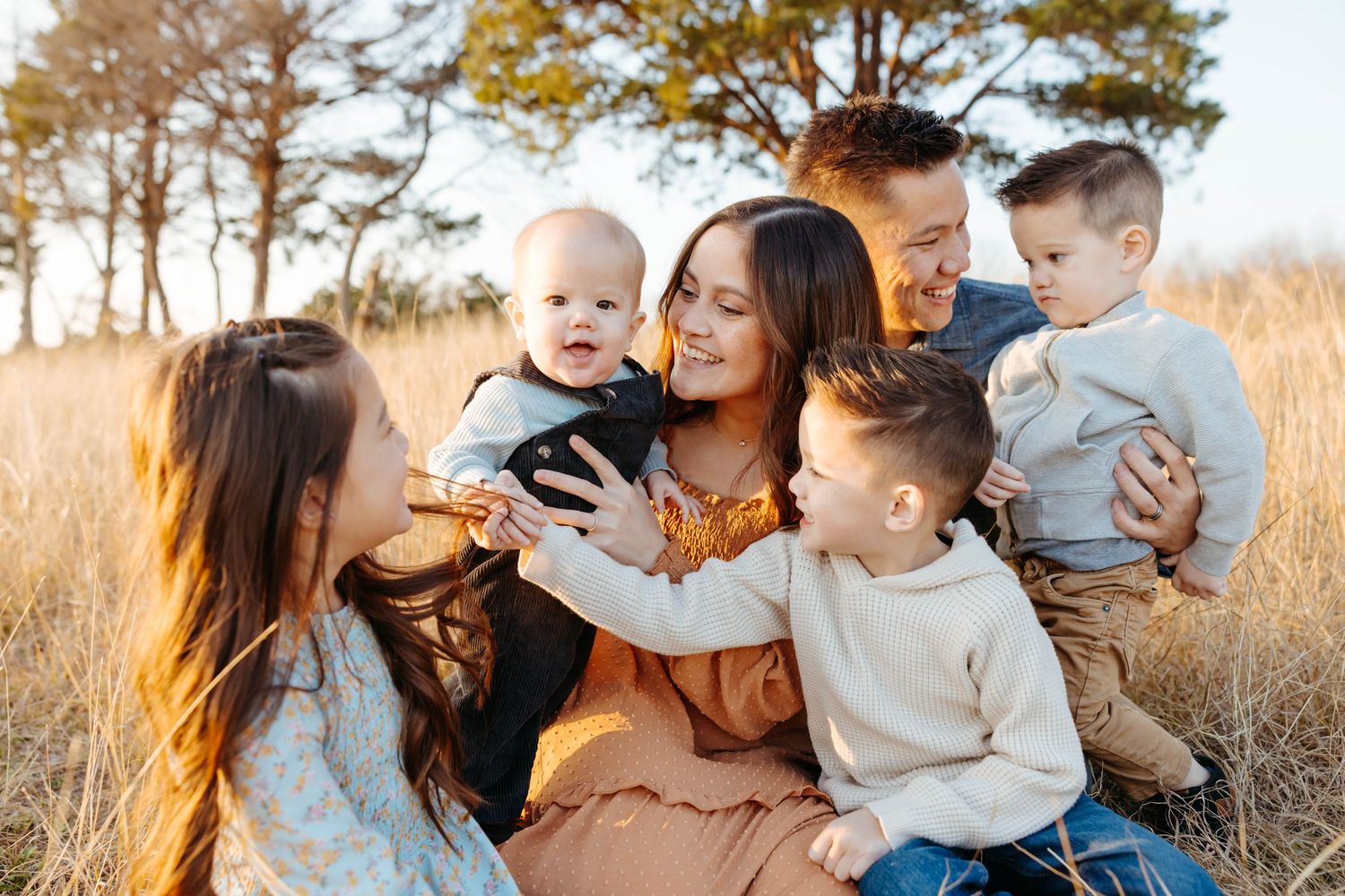 Family sharing tender moments together in a golden sunlit field during sunset.