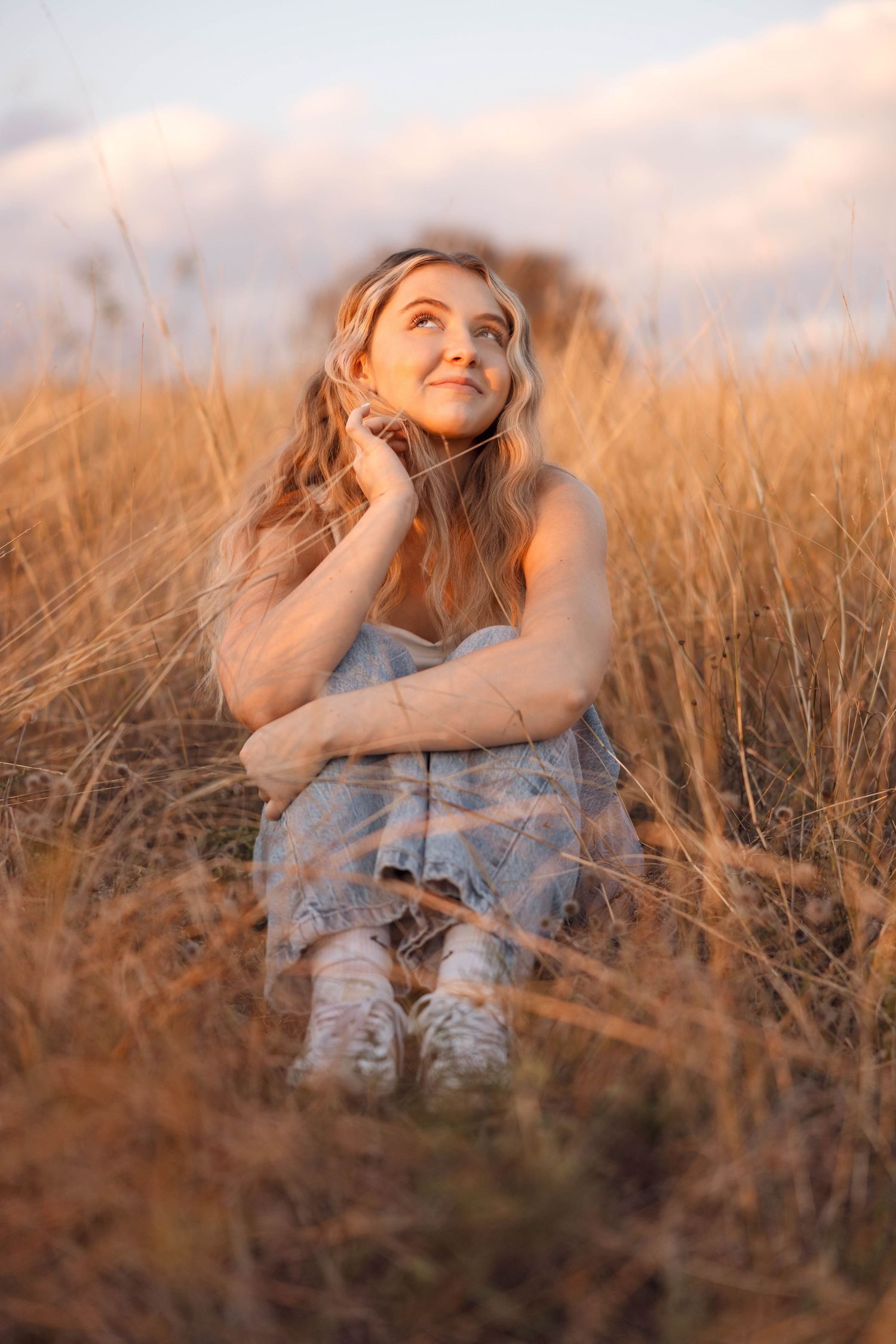 A person in a floral dress sits thoughtfully in a golden wheat field at sunset, bathed in warm evening light.