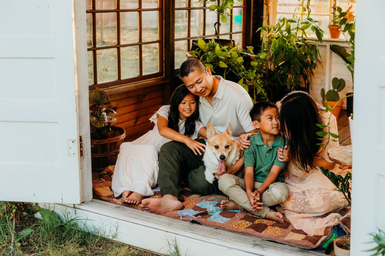 Family sitting on a quilt inside a greenhouse in Howe, Texas, smiling together during a lifestyle family photo session.
