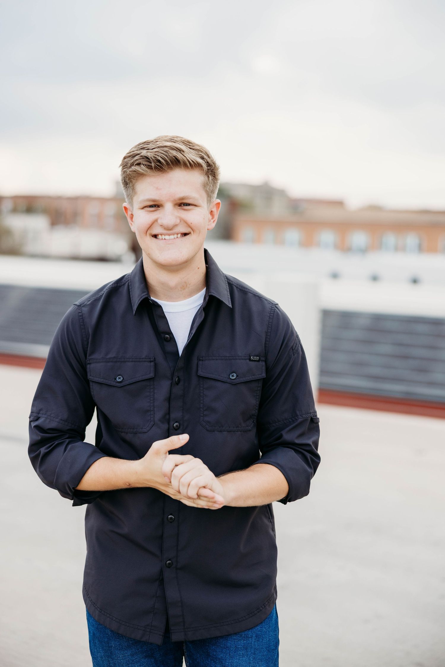 A person in a dark button-up shirt poses for a series of casual outdoor portraits on a rooftop setting.