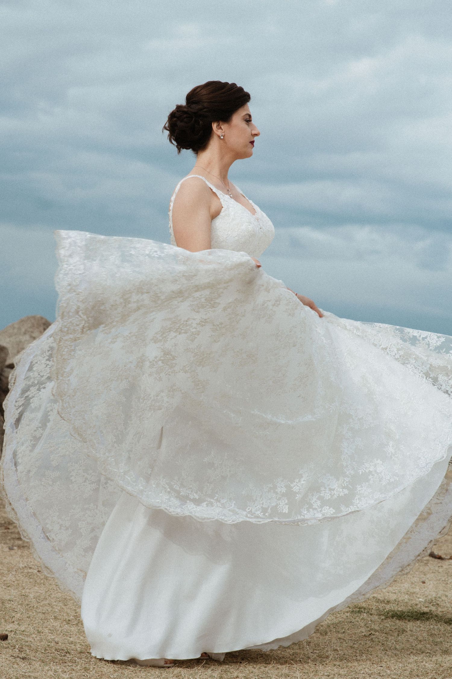 White lace wedding dress flowing in the wind against a cloudy sky.