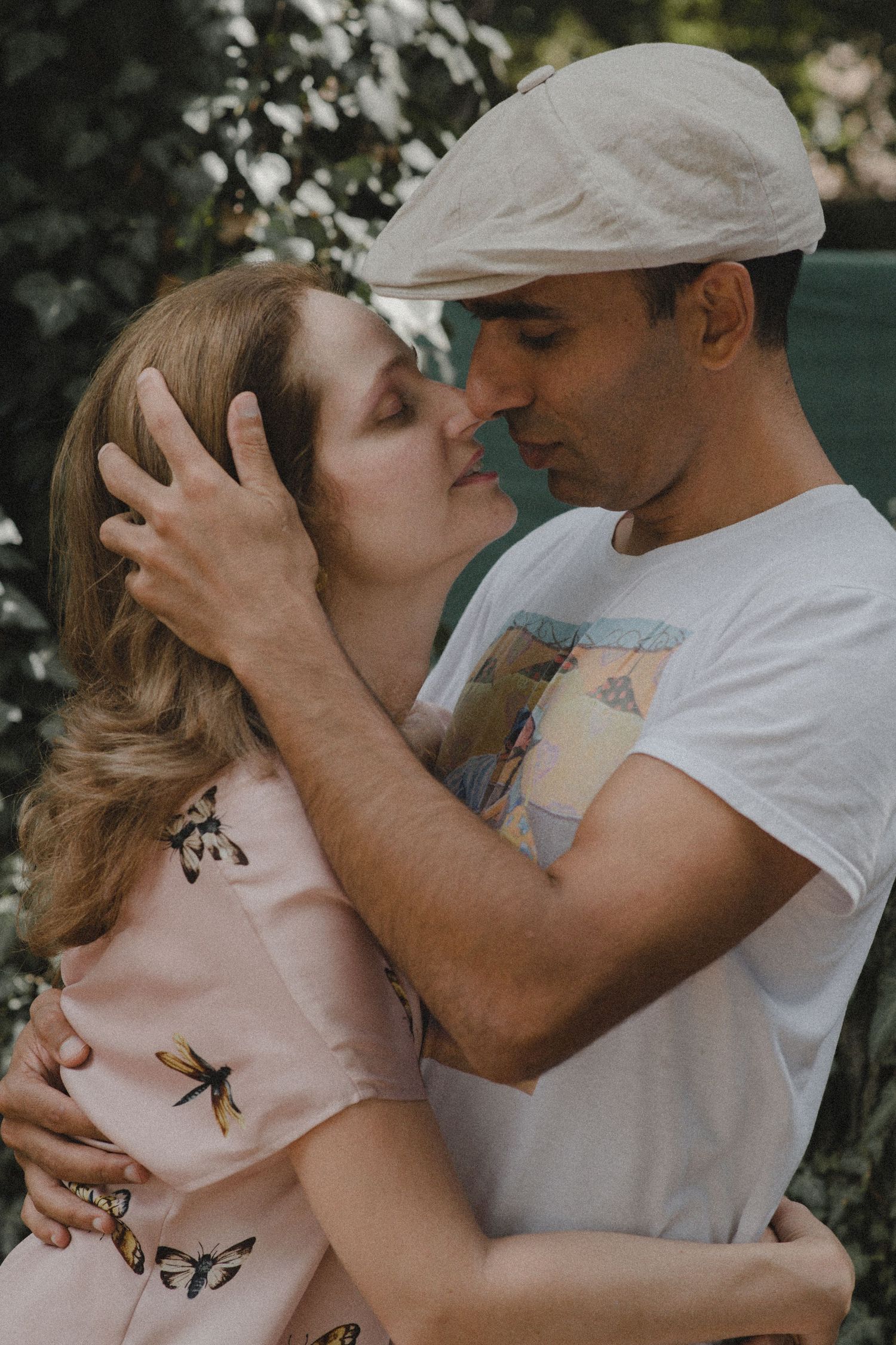 A romantic couple embraces in a garden setting with soft lighting and natural foliage in the background.