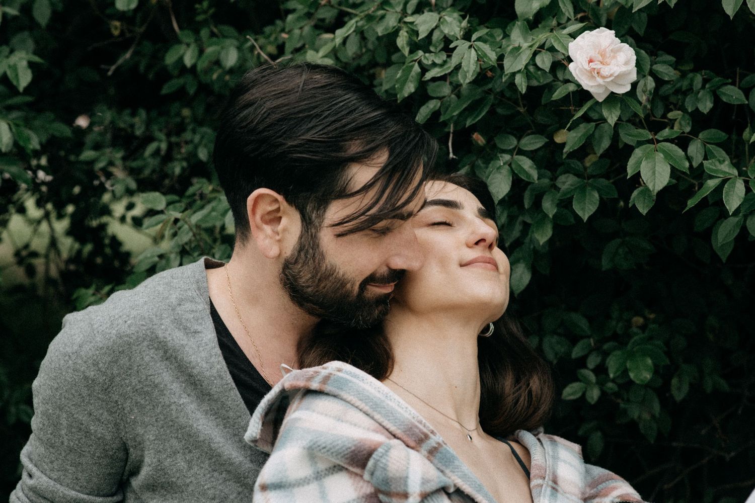 Romantic couple among rose bushes and greenery sharing an intimate moment.