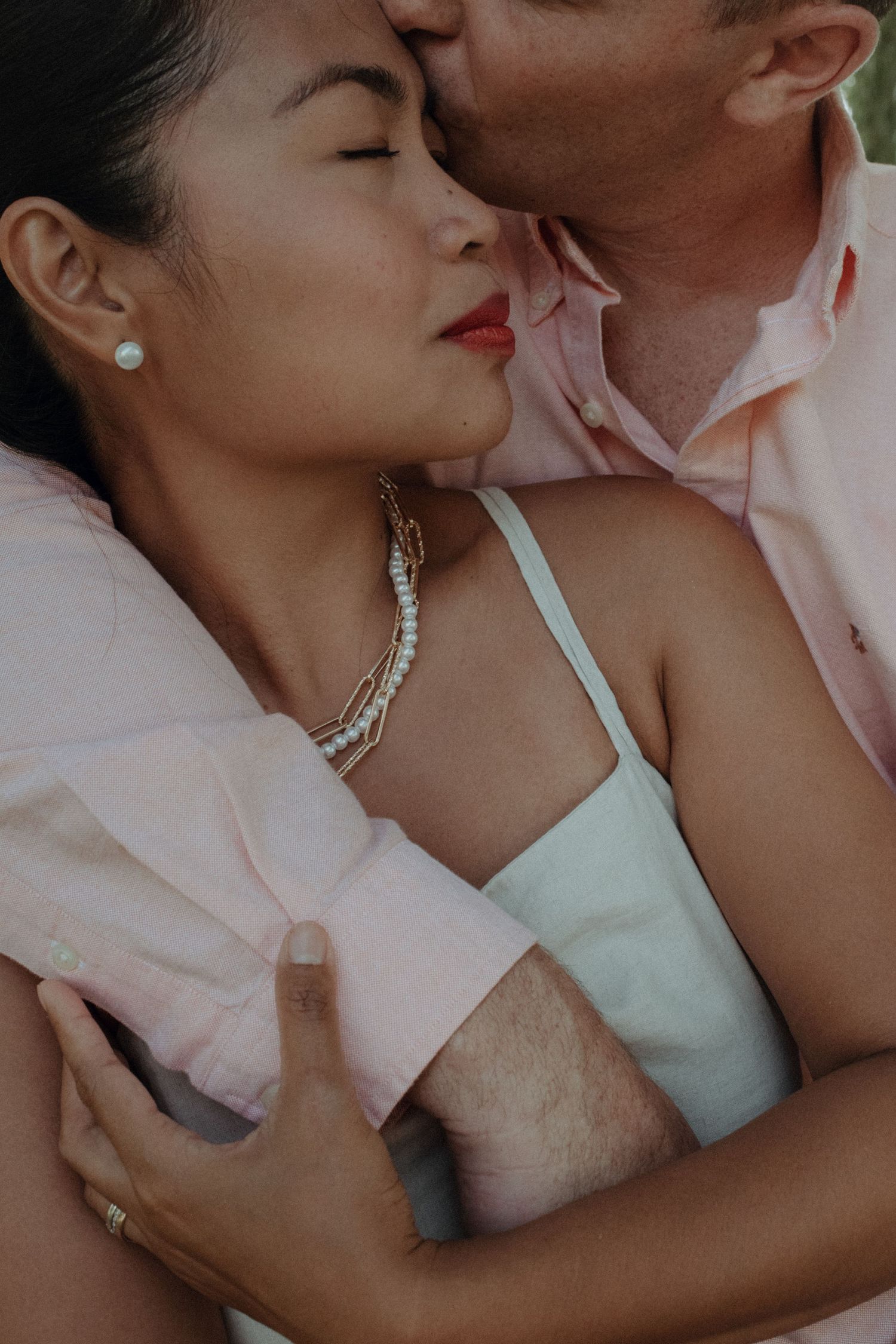 Intimate portrait of a couple in soft lighting with delicate jewelry and pastel clothing.