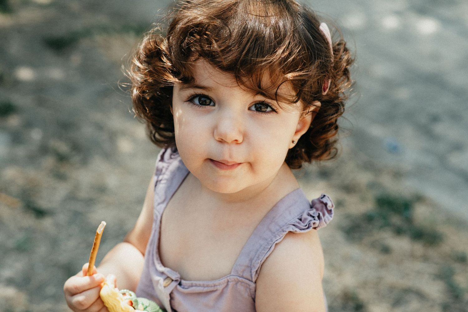 Small child wearing purple clothing plays outdoors near water.