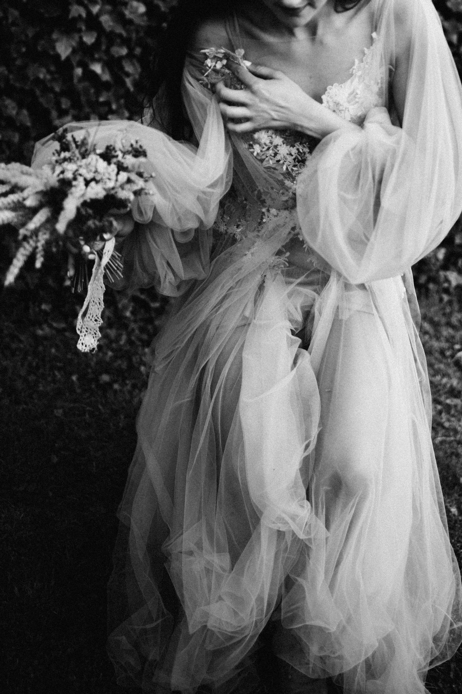 Ethereal black and white photo of someone in a flowing wedding dress holding a delicate bouquet.