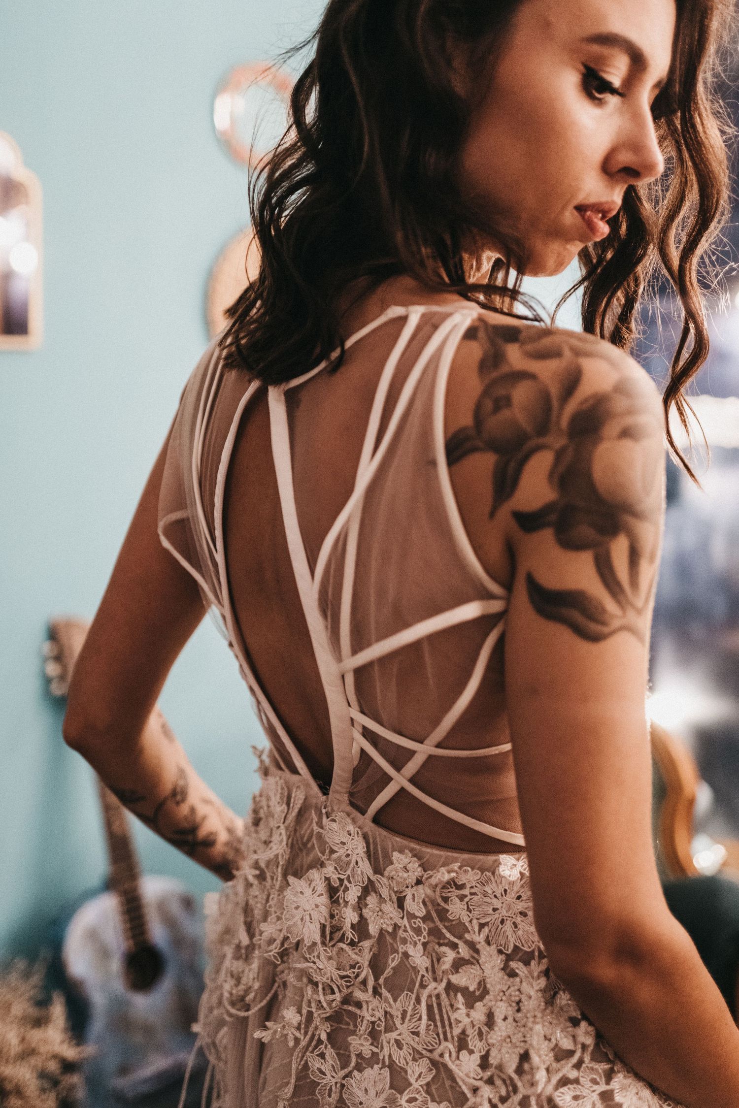 Back view of a lace wedding dress with intricate strappy details and visible tattoo art.