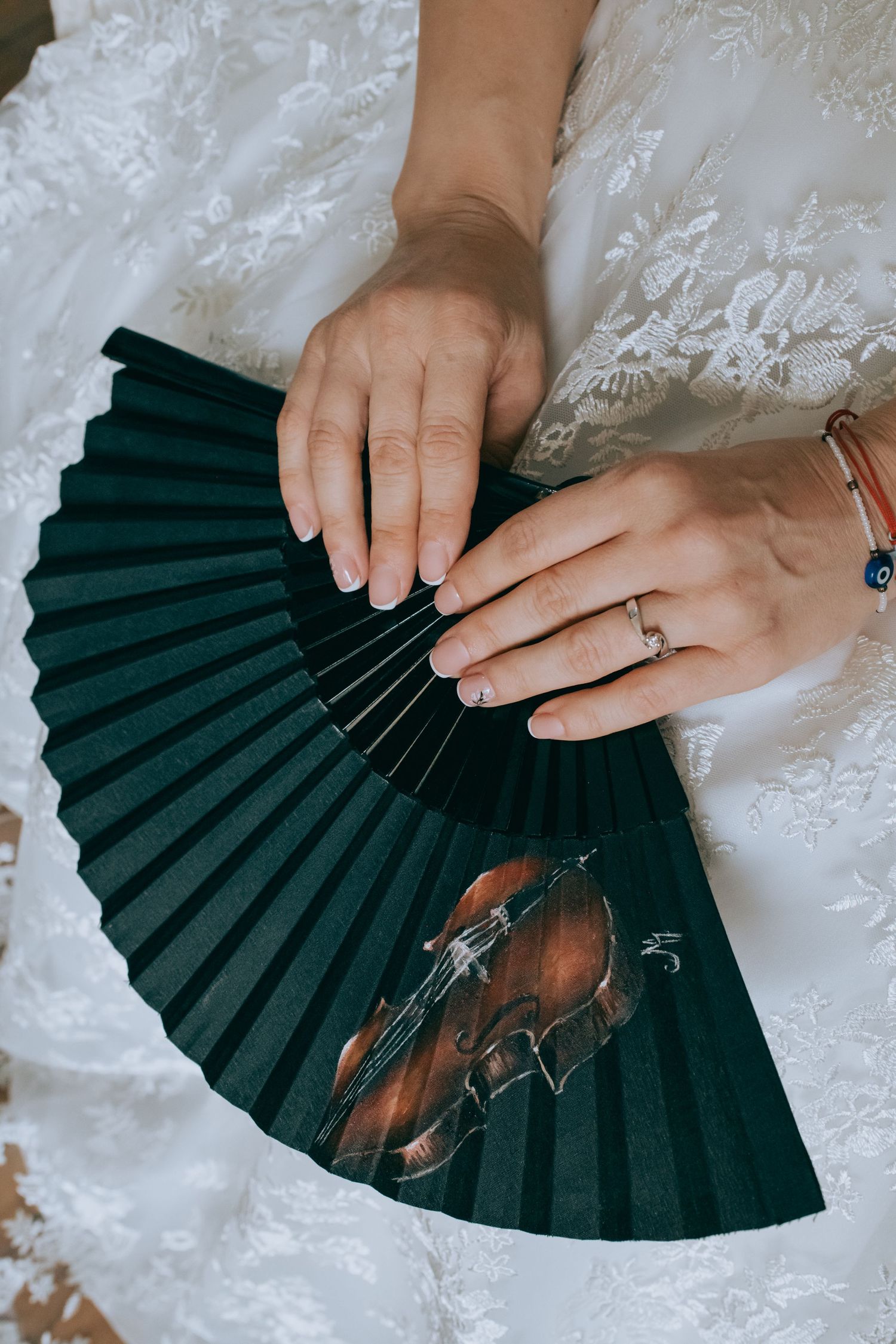 Hands delicately holding a dark green folding fan against white lace fabric.
