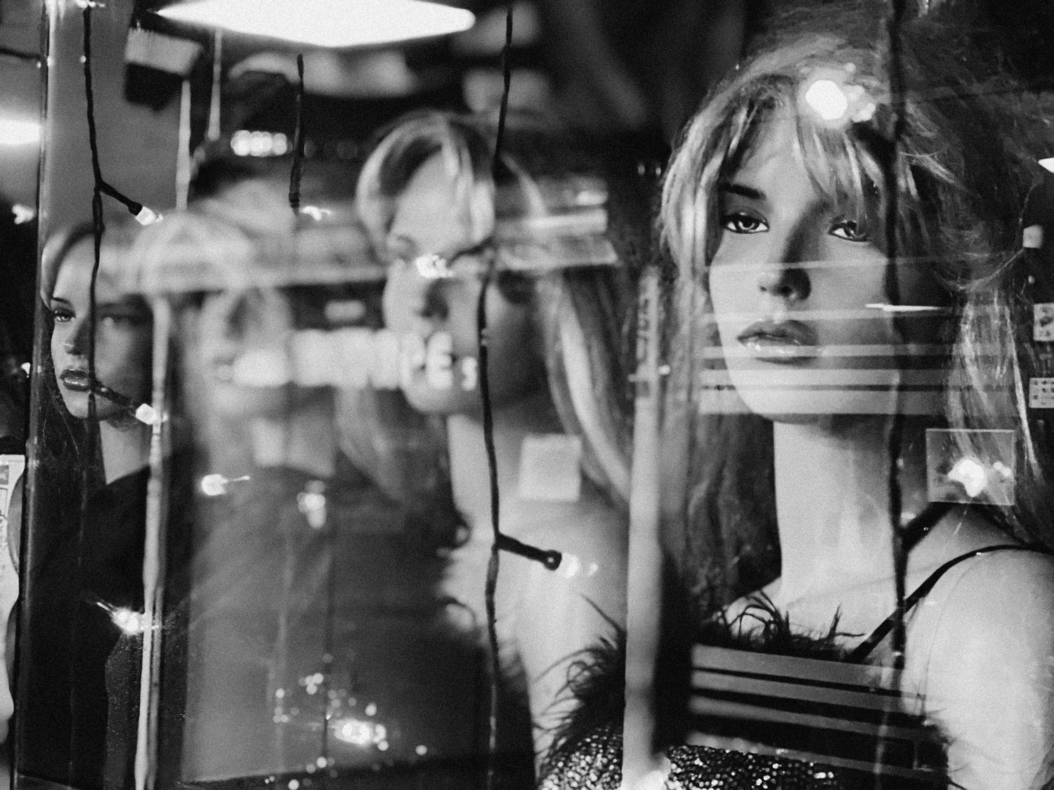 Display window mannequin behind glass with reflections creating layered black and white composition.