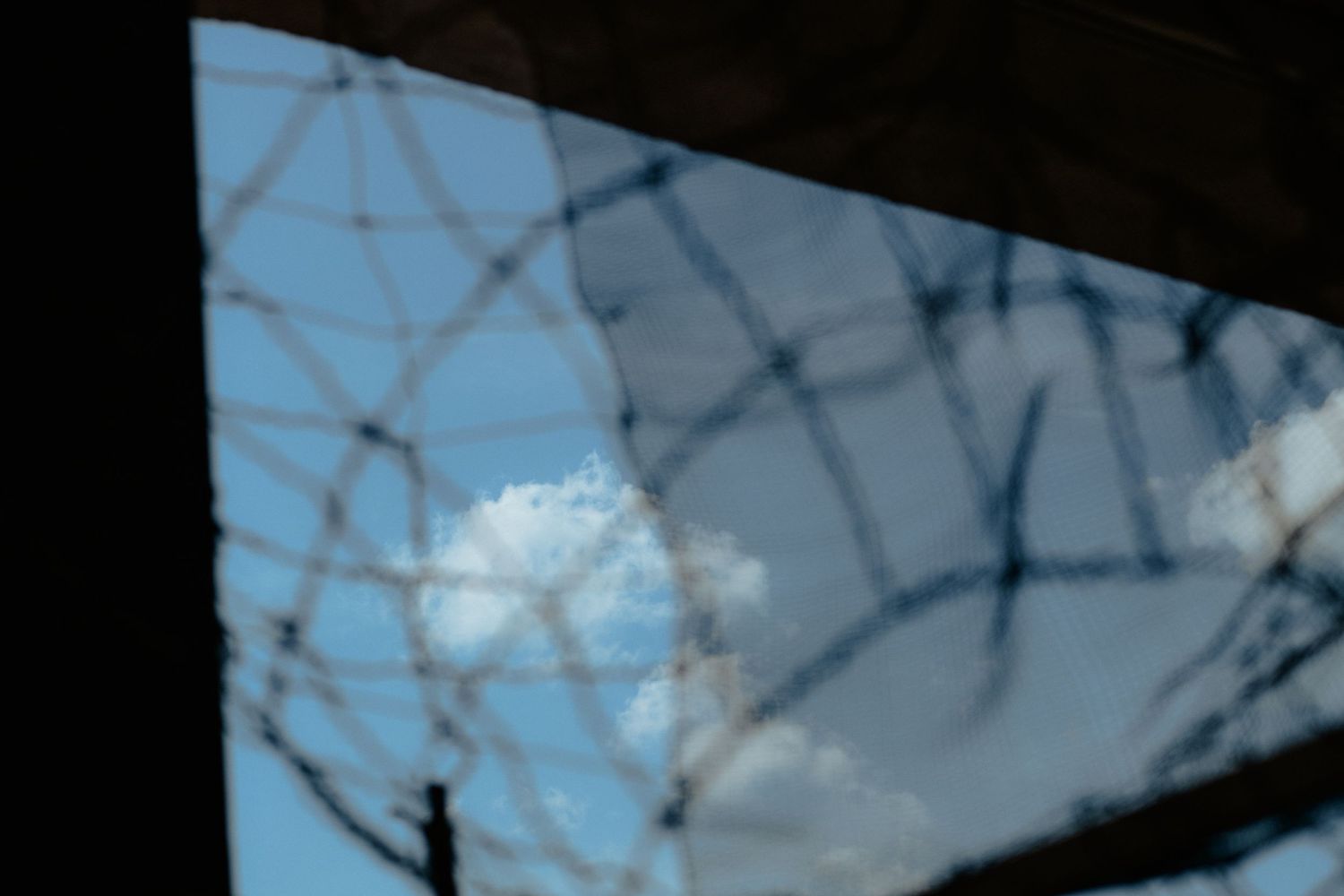 Cracked windshield pattern against a blue sky with white clouds.