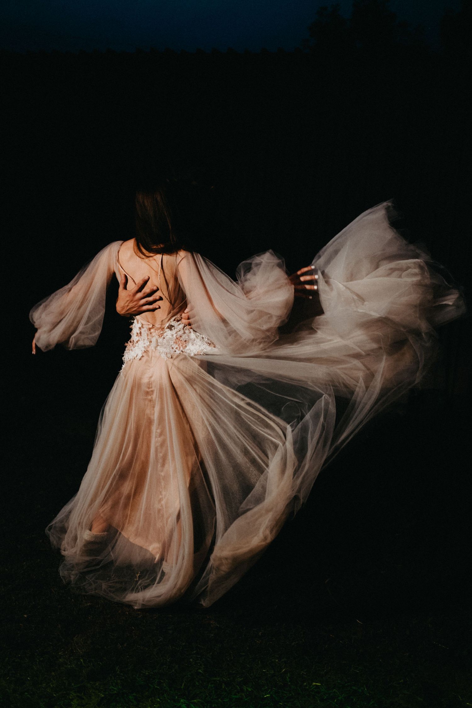 Flowing champagne-colored wedding dress captured in motion against a dark background.