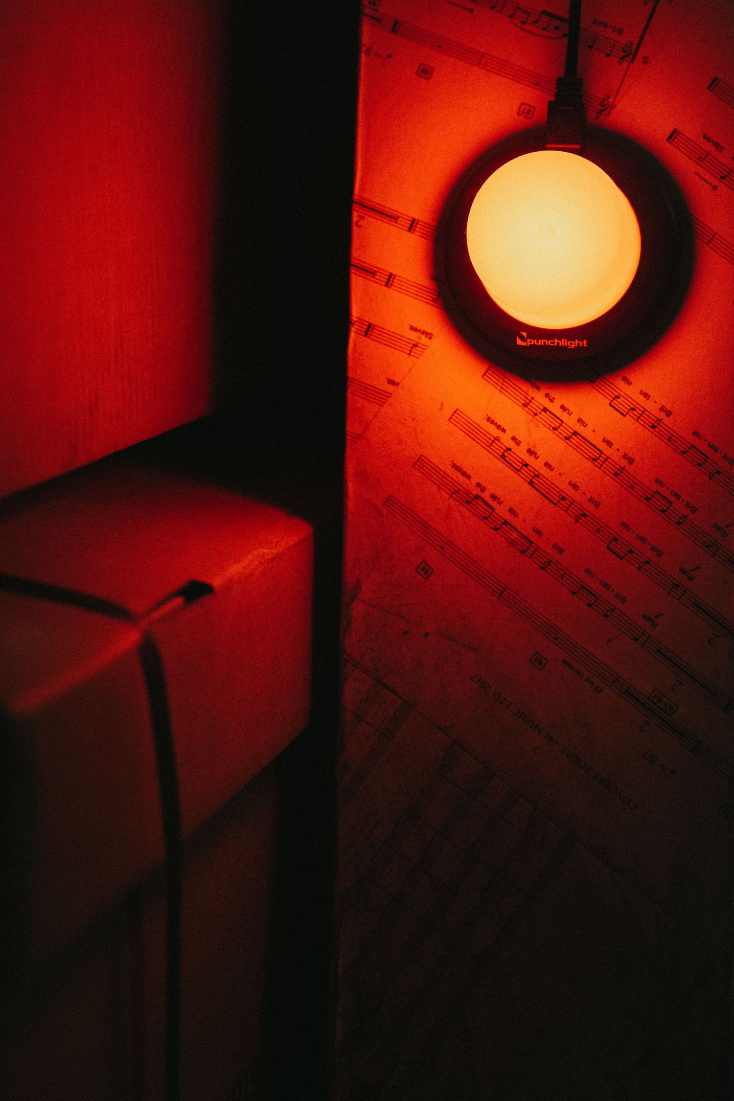 Moody red lighting illuminates a hanging lamp and text on paper creating dramatic shadows and atmosphere.