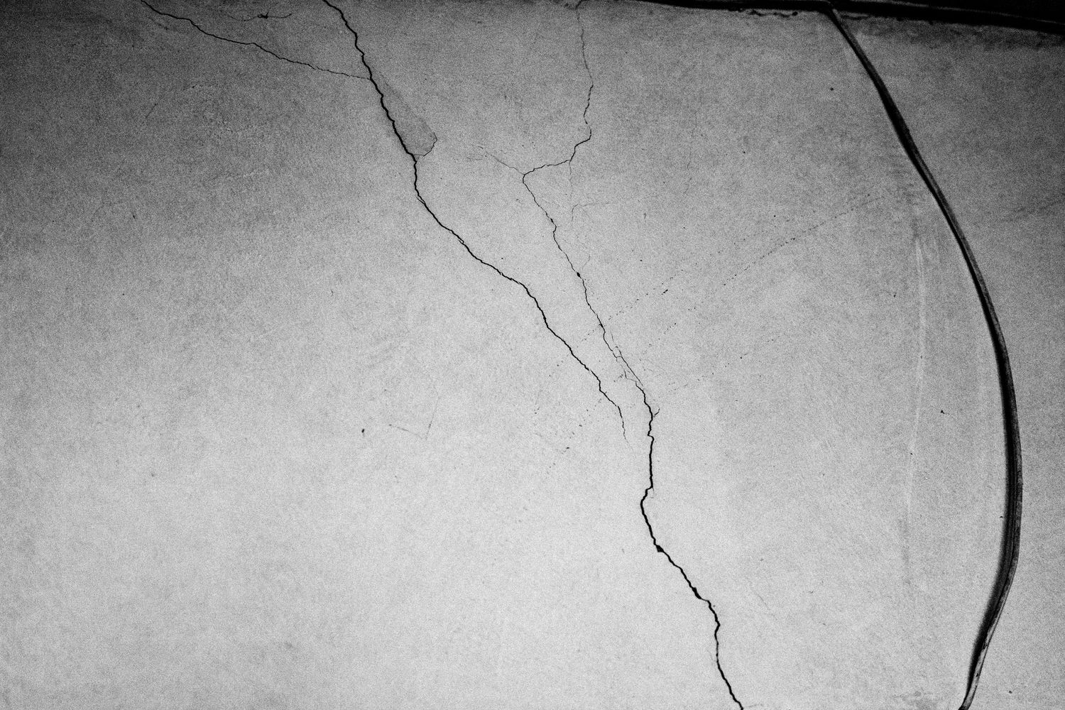 Abstract black and white photograph of cracks spreading across a textured wall surface.