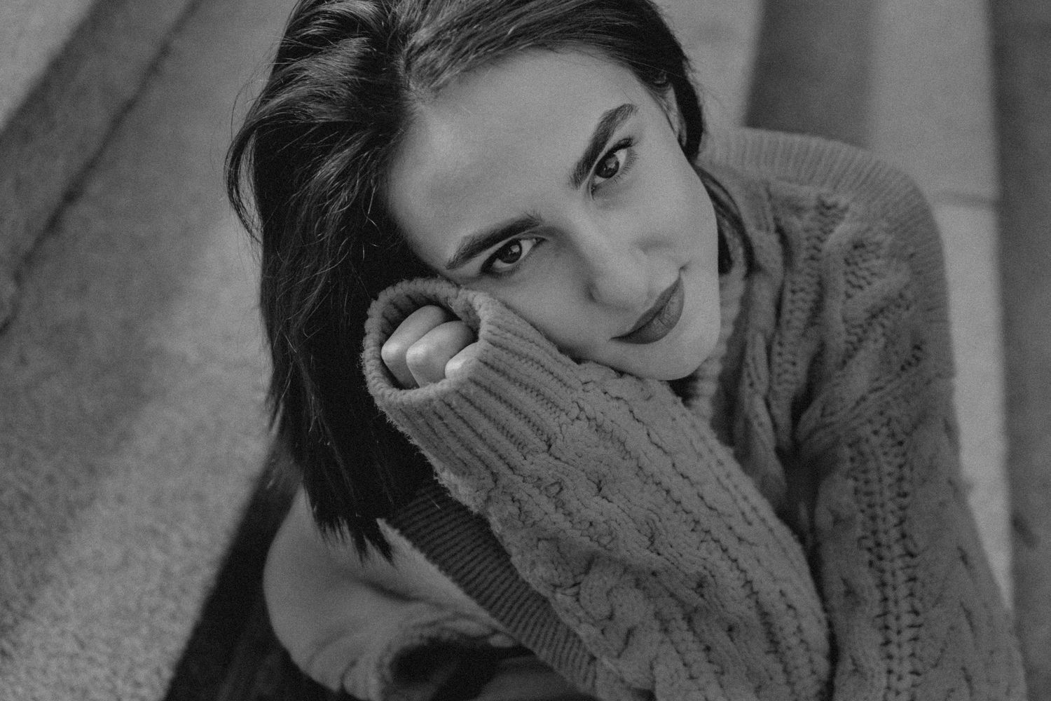 A black and white portrait of someone wearing a chunky knit sweater looking at camera with a gentle expression.